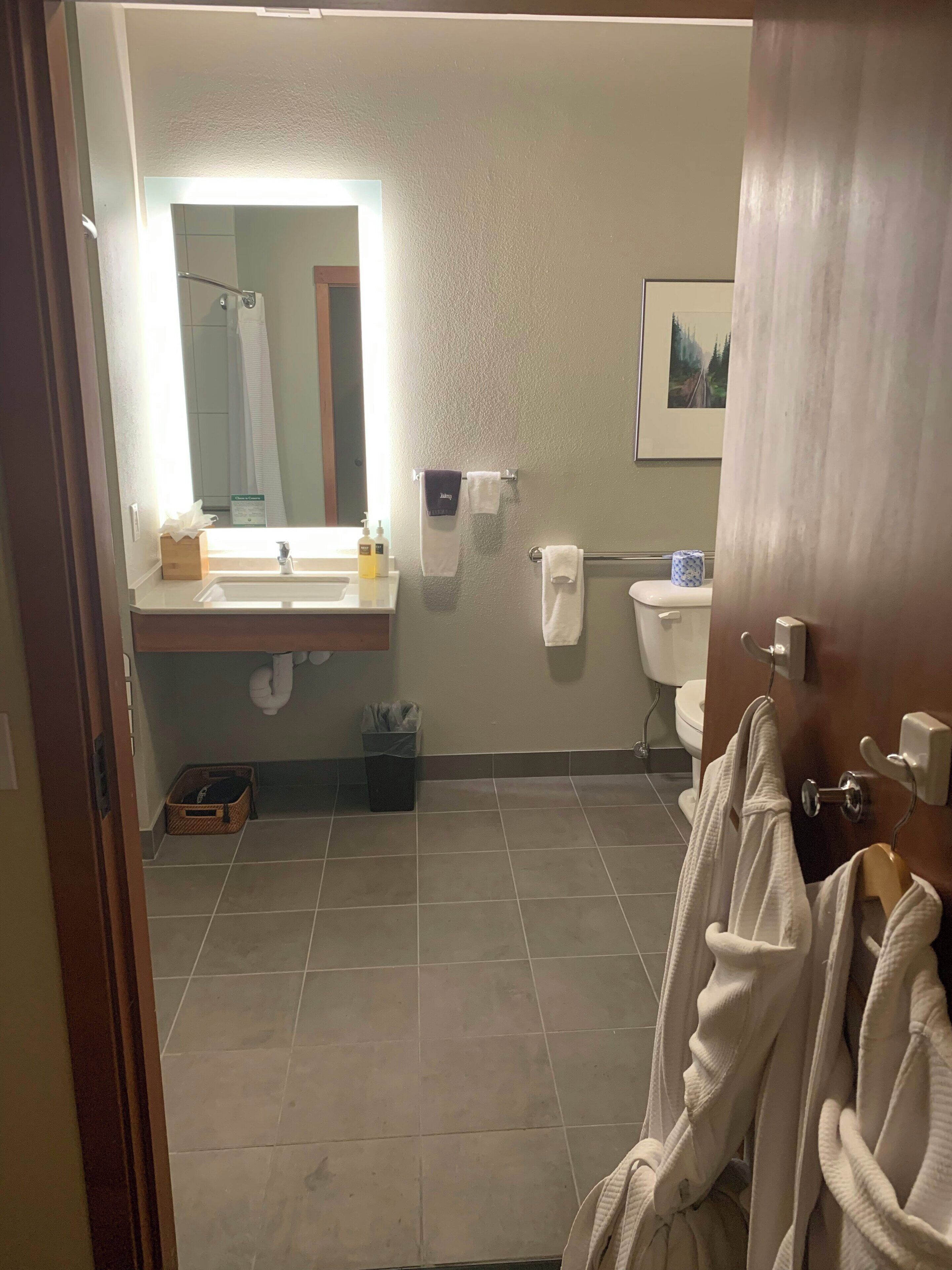 A bathroom with a sink, mirror, towel rack, toilet, and a door with a towel hanging.
