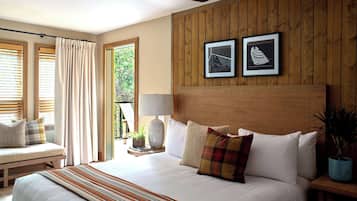 A bedroom with a large bed, a ceiling fan, wooden panel walls, and two framed artworks.