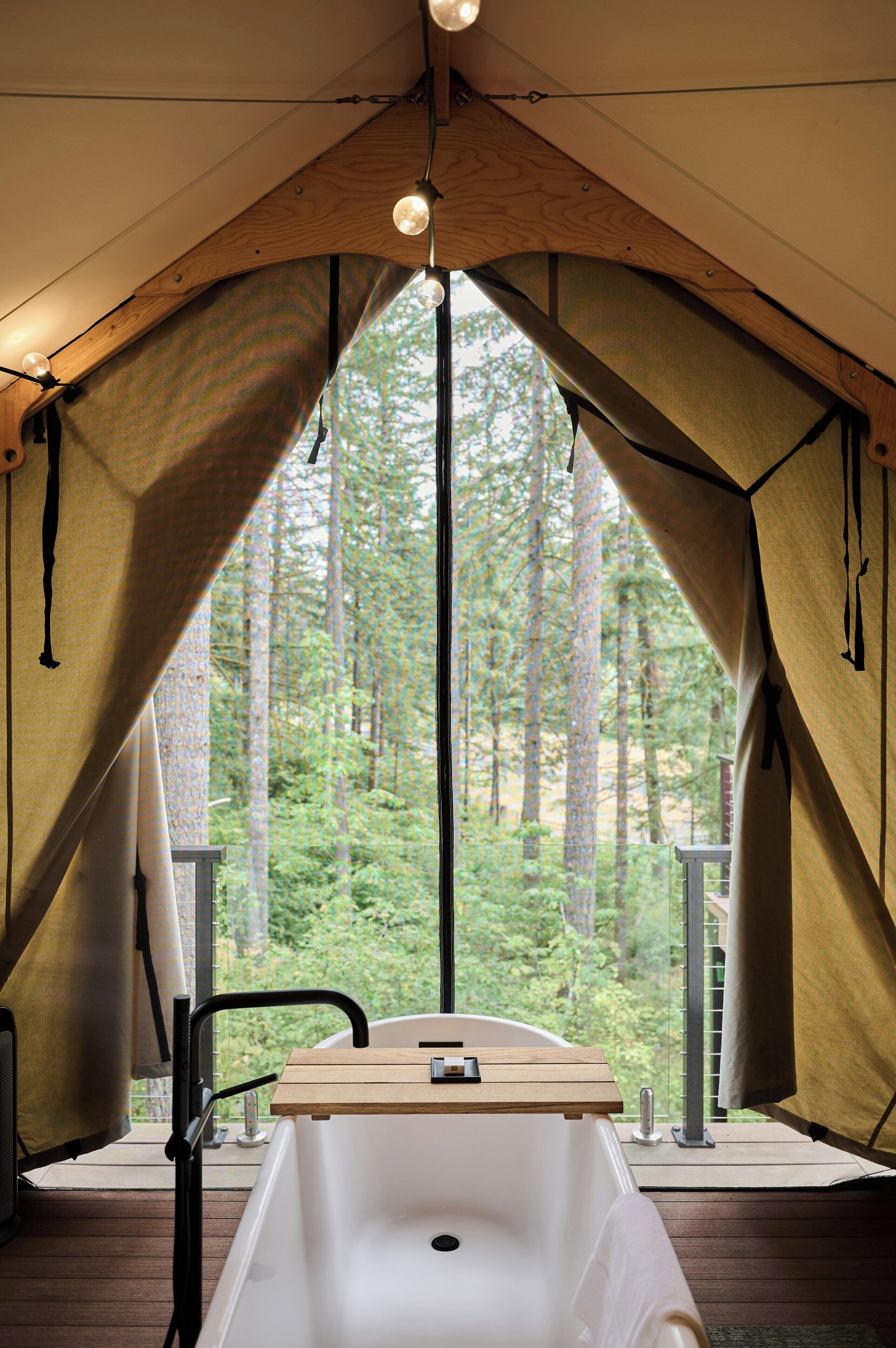 Une cabane aménagée avec une terrasse en bois, une baignoire et une vue sur une forêt.