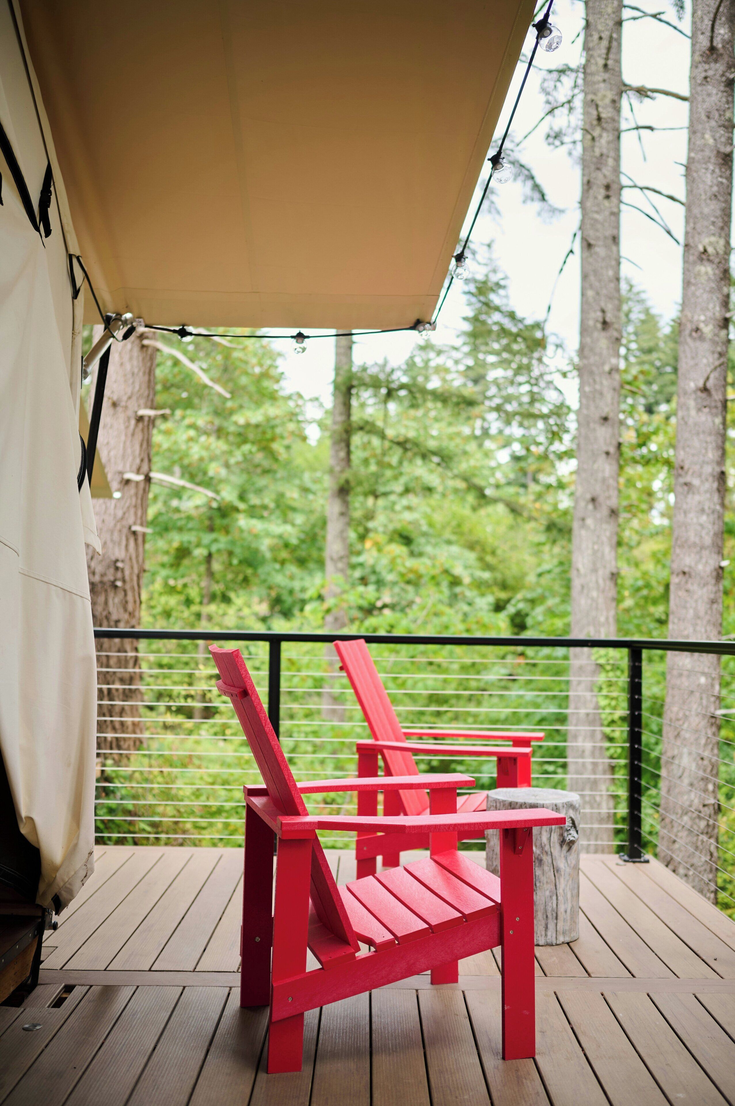 Une terrasse en bois avec des fauteuils Adirondack rouges placés sous une tonnelle.