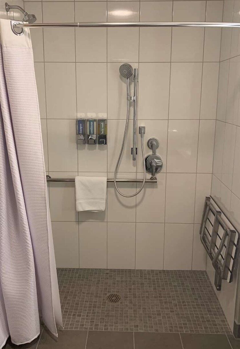 Un espace douche équipé d’un pommeau de douche à main, d’un porte-serviettes avec une serviette blanche et d’un présentoir mural pour les articles de toilette.
