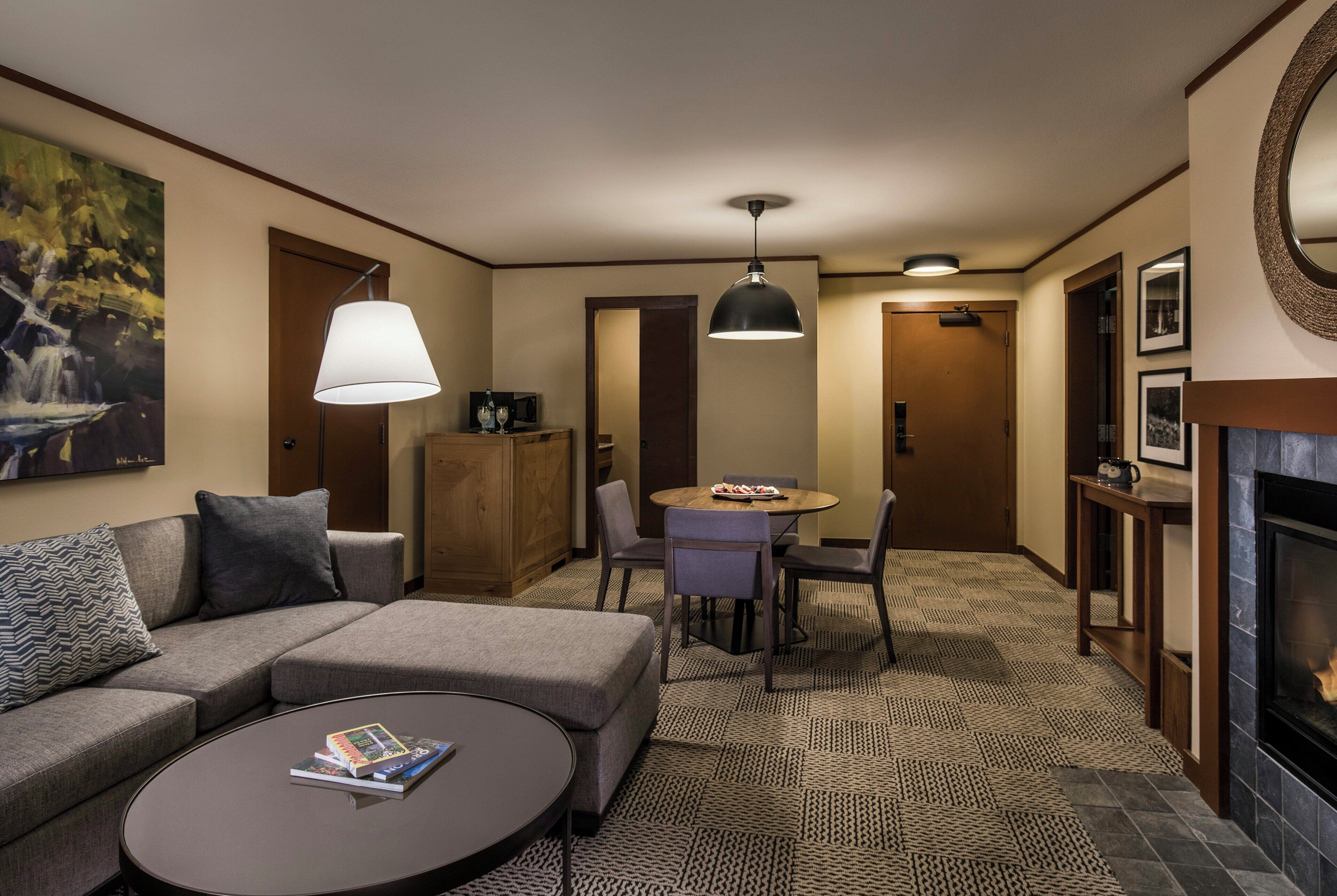 A hotel room with a sofa, a dining table with chairs, a fireplace, and a painting on the wall.