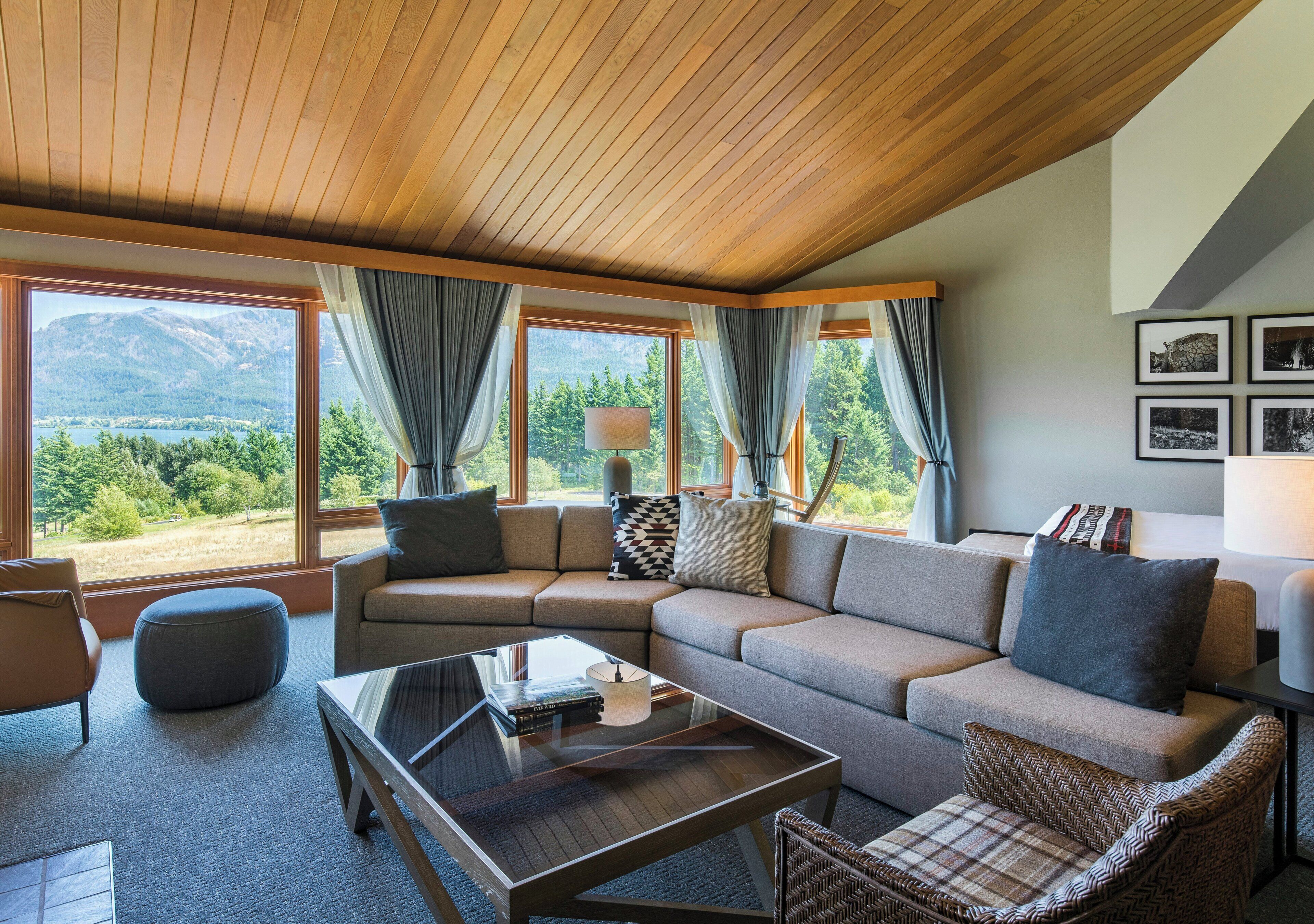 A modern living room with a sectional sofa, a glass coffee table, and a view of a mountainous landscape through large windows.