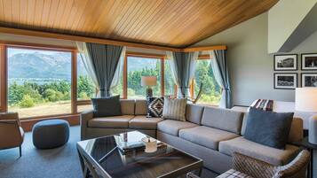 A modern living room with a sectional sofa, a glass coffee table, and a view of a mountainous landscape through large windows.