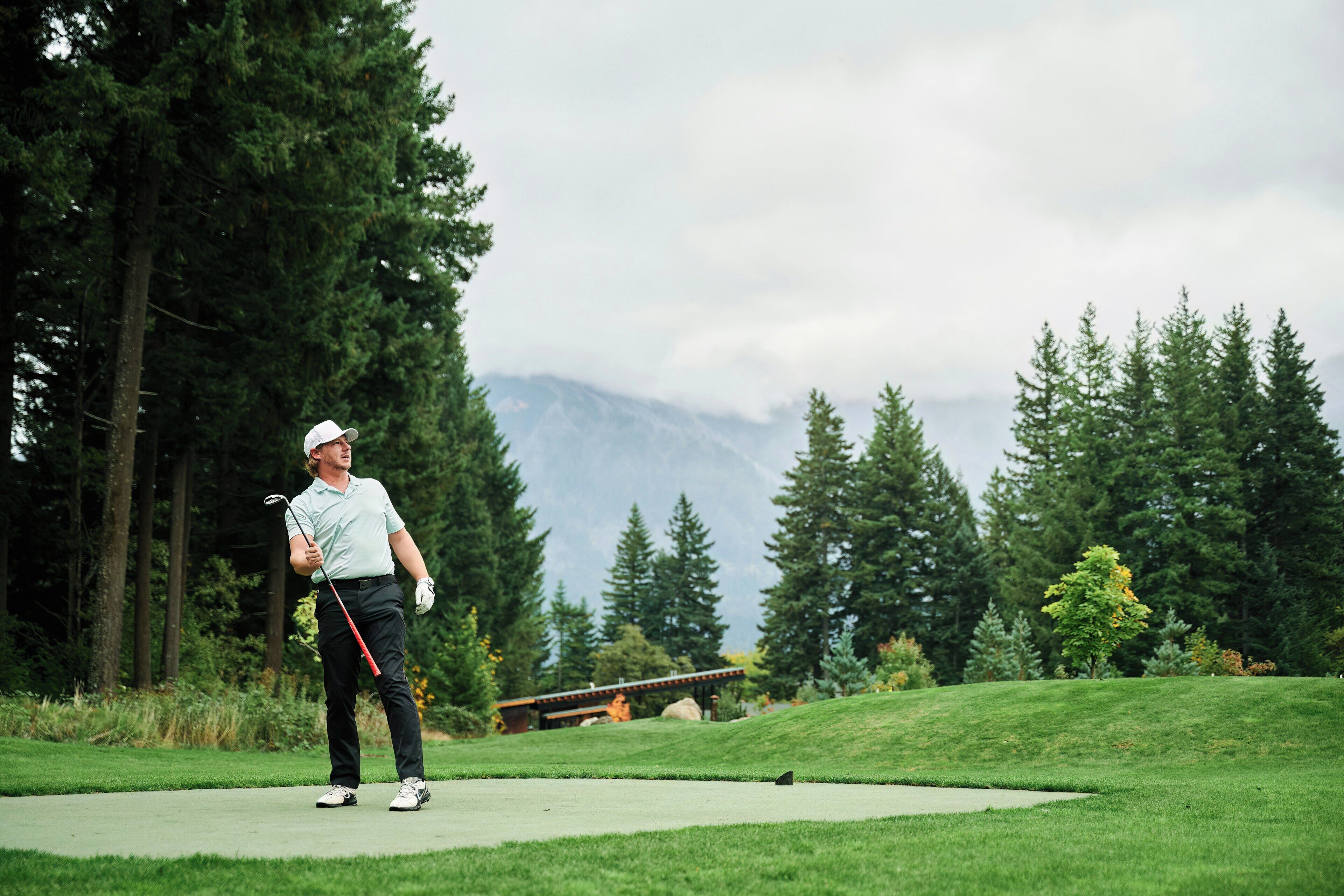 A person on a golf course with a view of mountains and trees in the background.