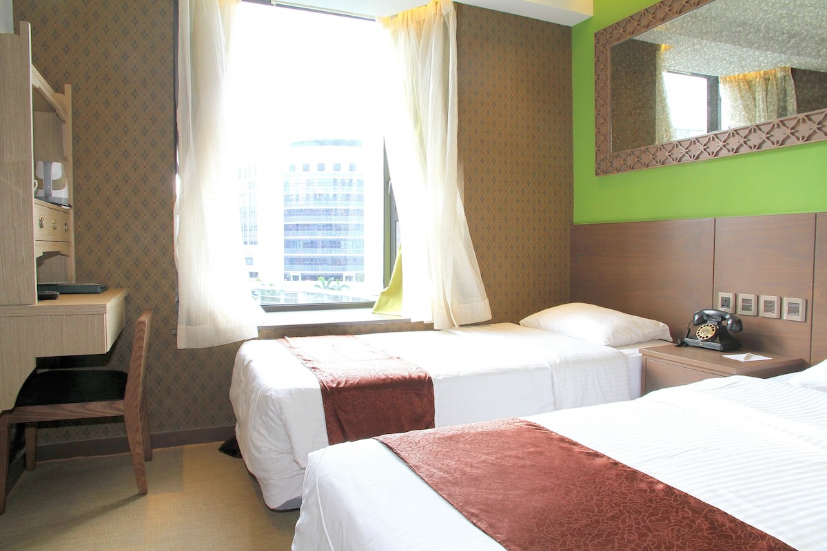 A hotel room with two beds, a desk, a chair, a telephone, and a window with curtains.