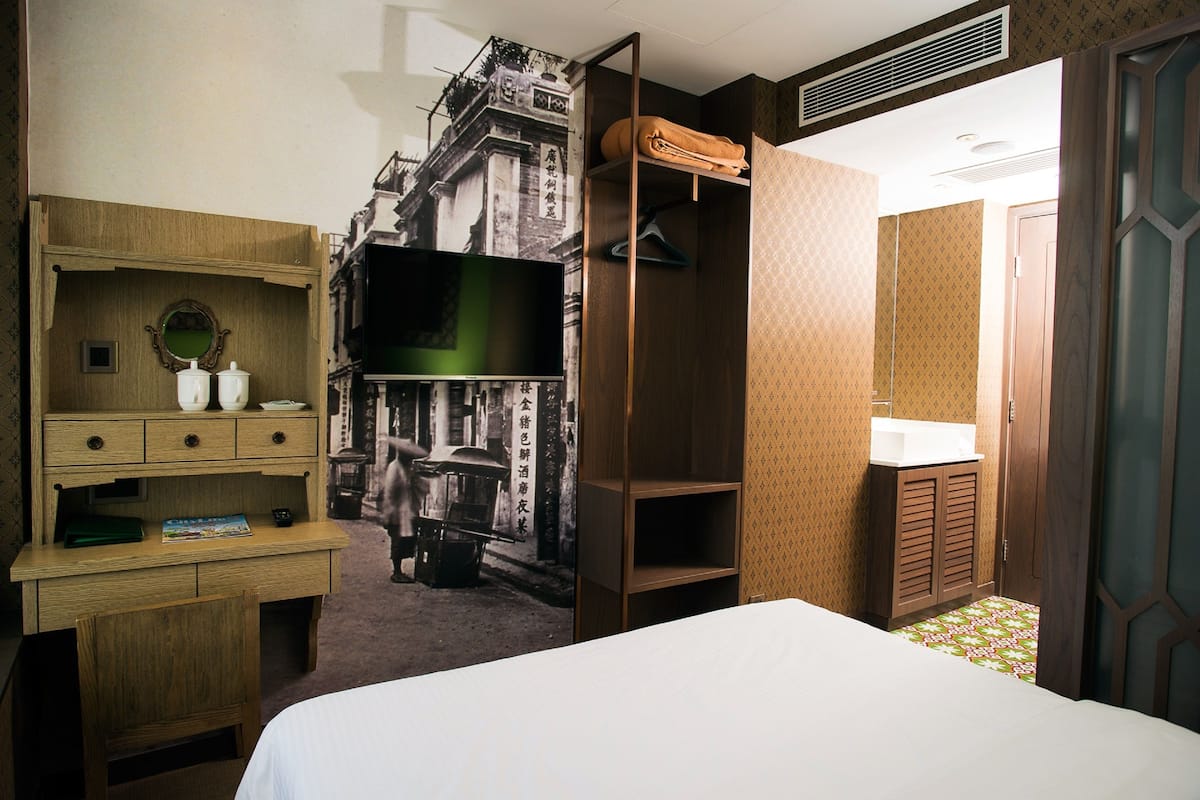 A hotel room with a bed, a wooden desk, a television, and a wardrobe.