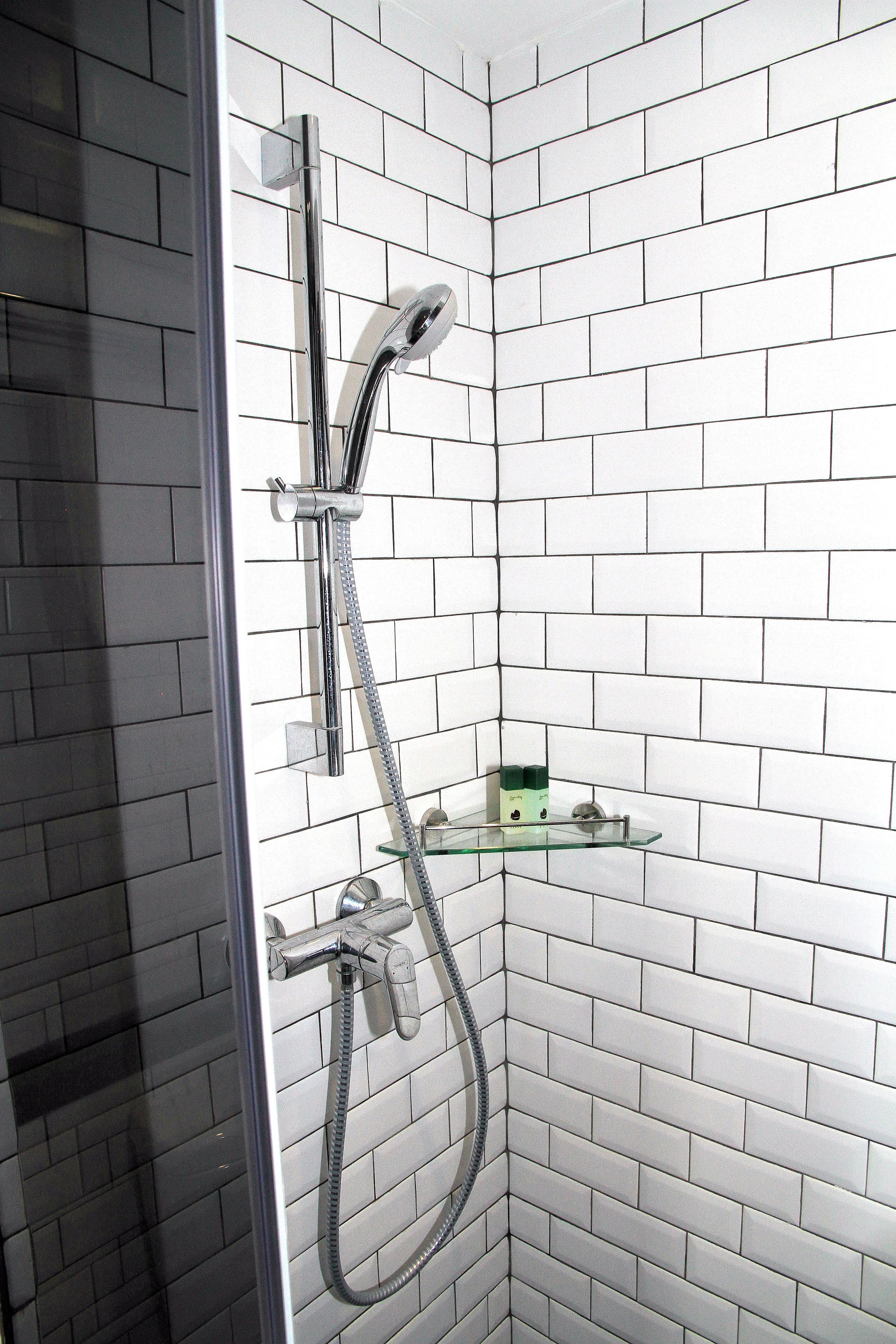 A corner shower with a glass shelf, chrome fixtures, and white tiled walls.
