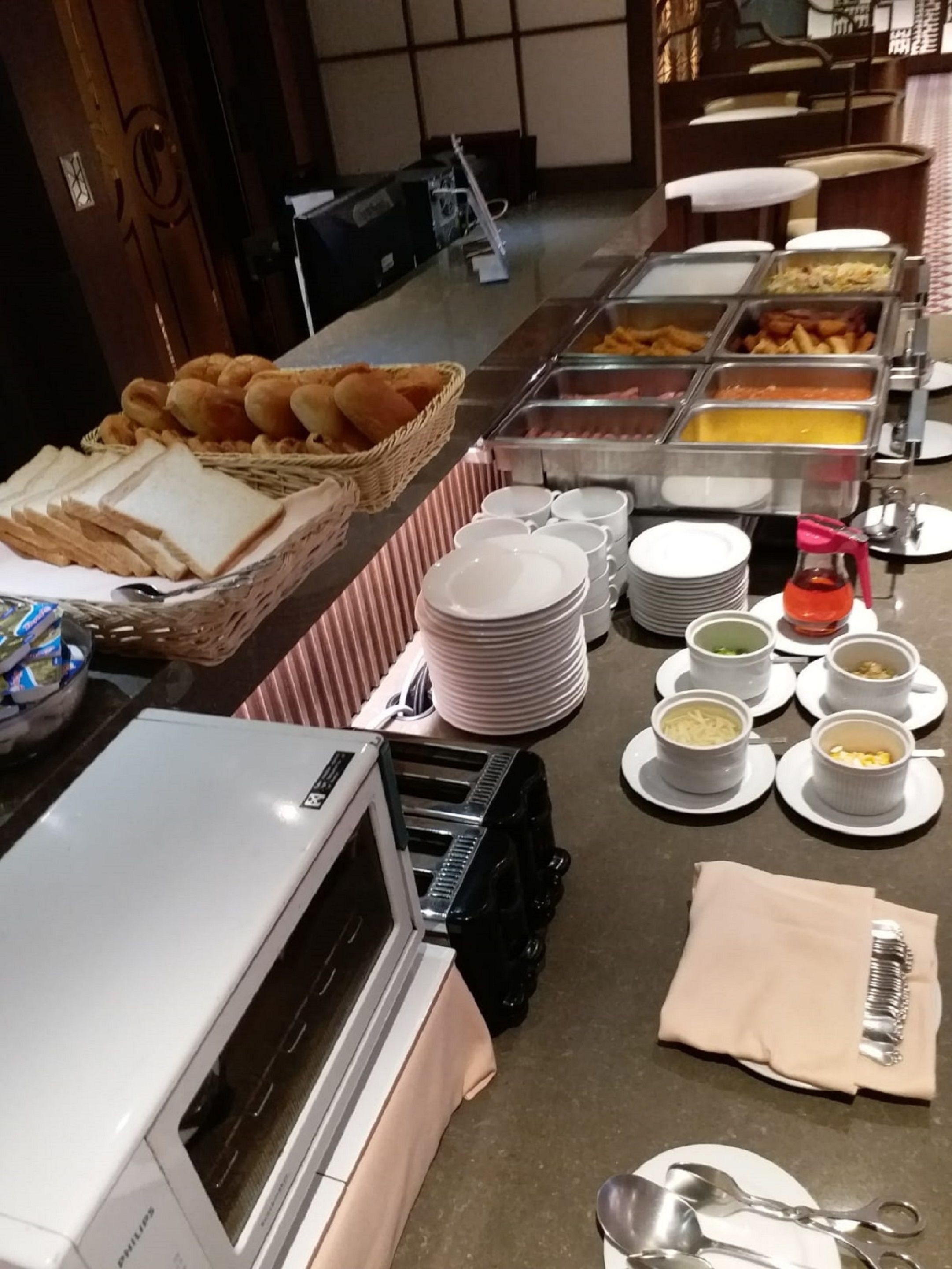 A buffet setup with bread, pastries, and various food containers.