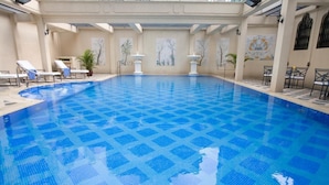 Una grande piscina al coperto con pavimento piastrellato blu, circondata da poltrone relax e tavolini.