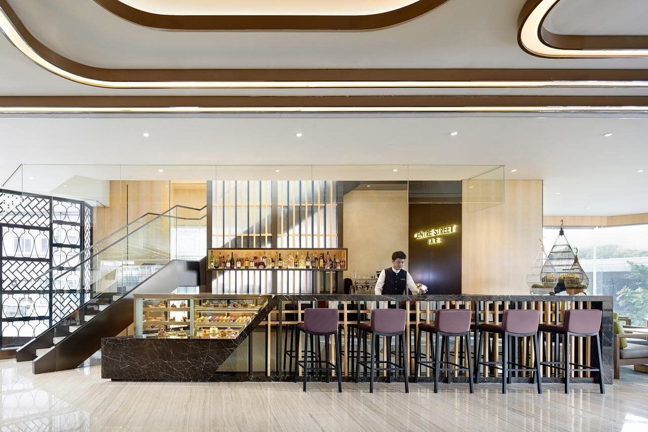 A modern bar area with a bartender, a staircase, and a display of bottles.