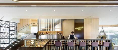 A modern bar area with a bartender, a staircase, and a display of bottles.