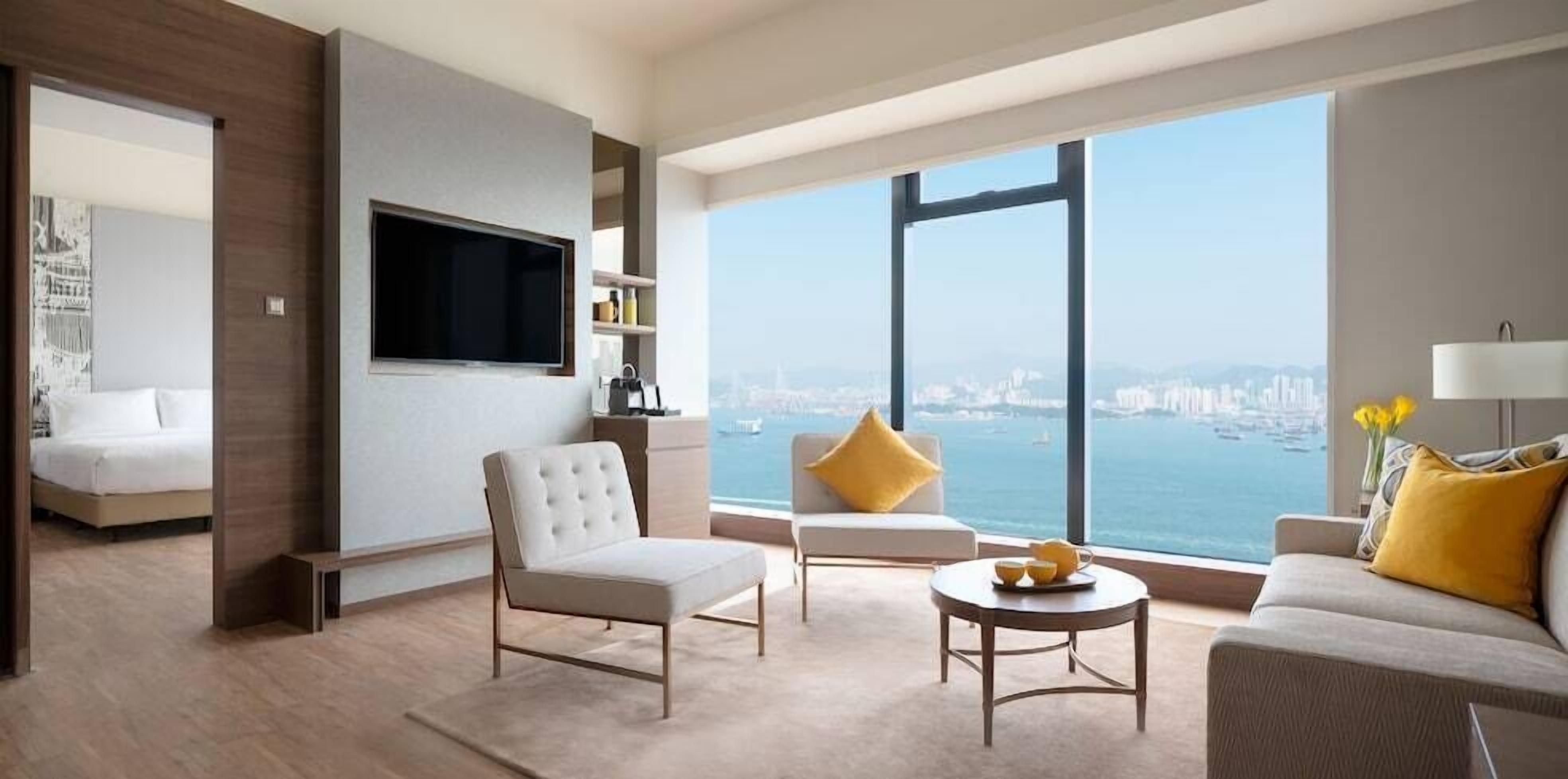 Ein modernes Wohnzimmer mit großem Fenster, einem Flachbildfernseher und einem Sofa mit gelben Kissen.