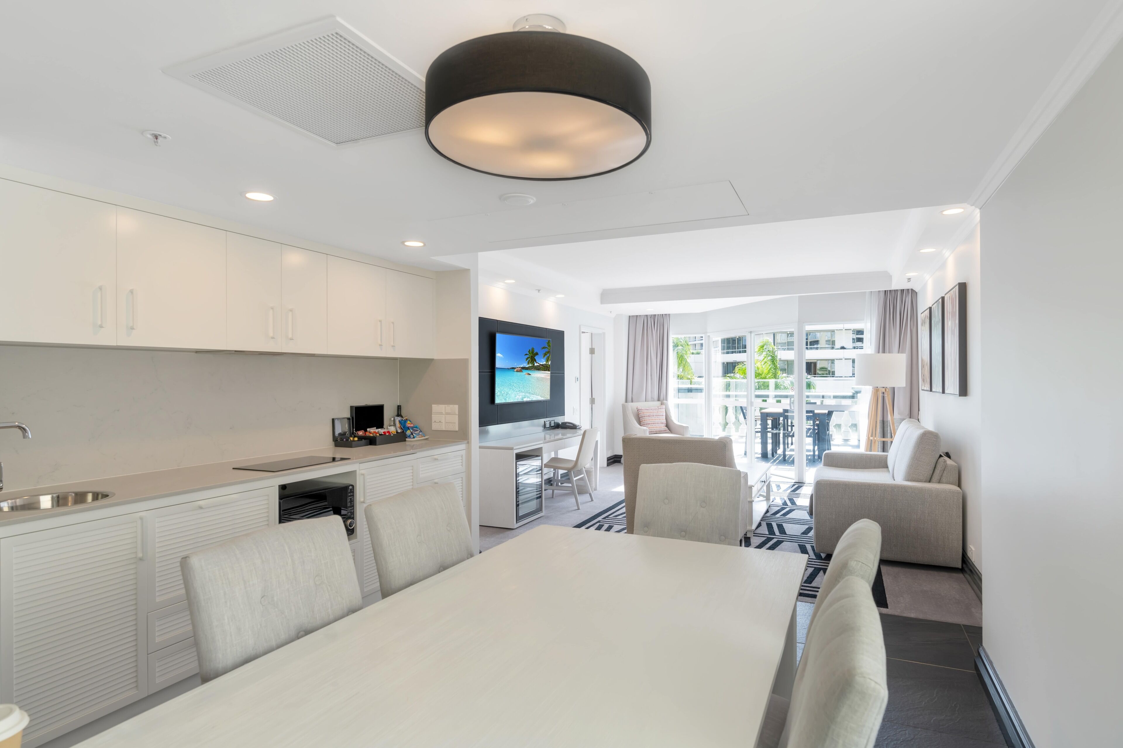 Una habitación de hotel moderna con zona de comedor, kitchenette y balcón con vistas a la ciudad.