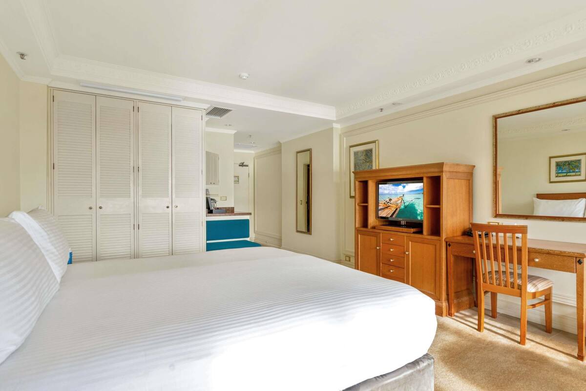 Une chambre d’hôtel avec un grand lit, un bureau avec une chaise, une télévision et une armoire.
