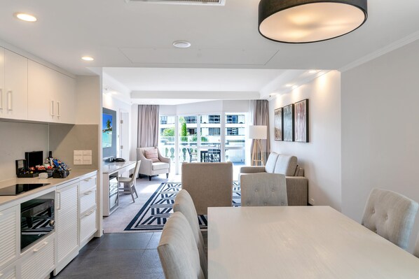 A modern hotel room with a dining area, kitchenette, and a view of the cityscape.