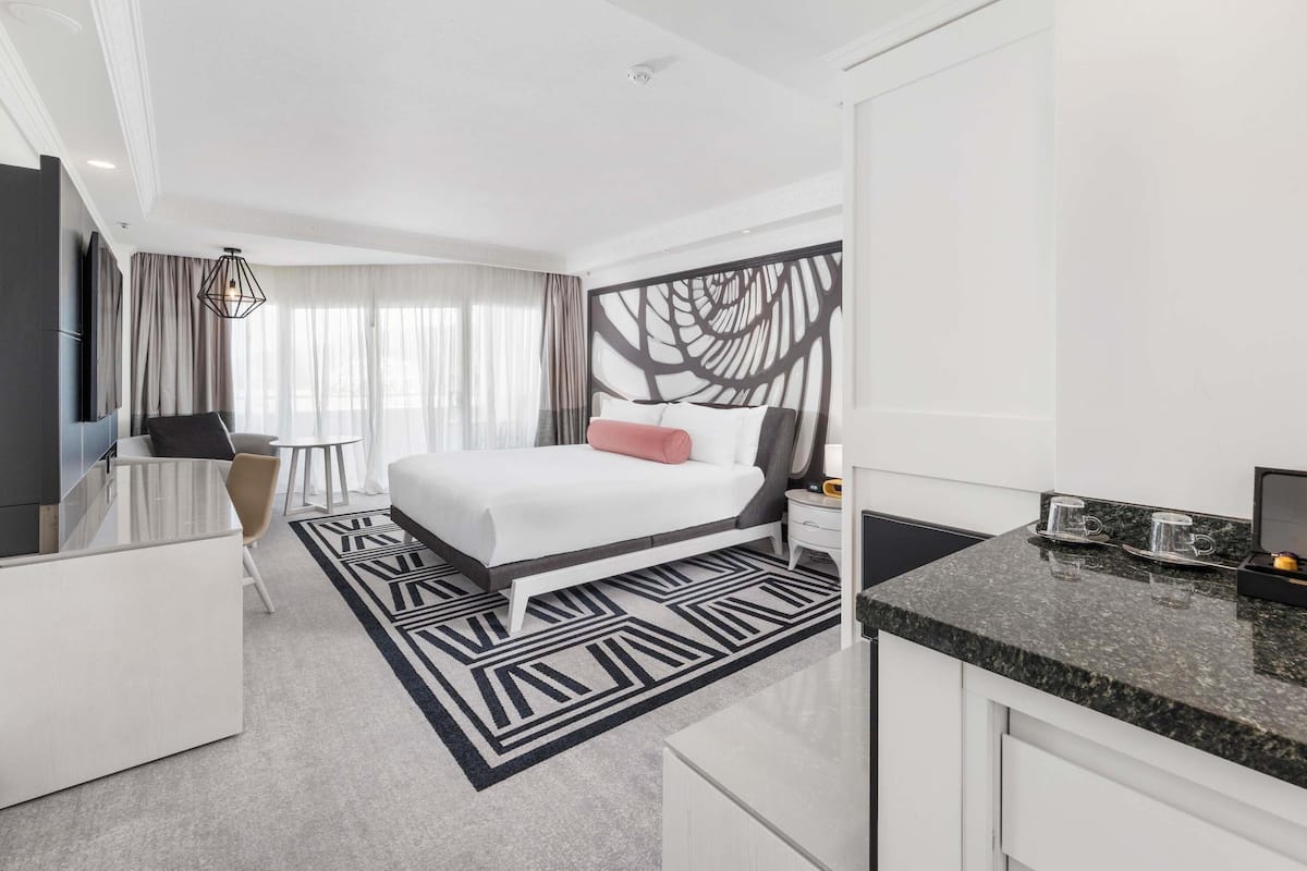 Une chambre d’hôtel moderne équipée d’un grand lit, d’un bureau, d’une chaise, d’une télévision et d’un coin cuisine.