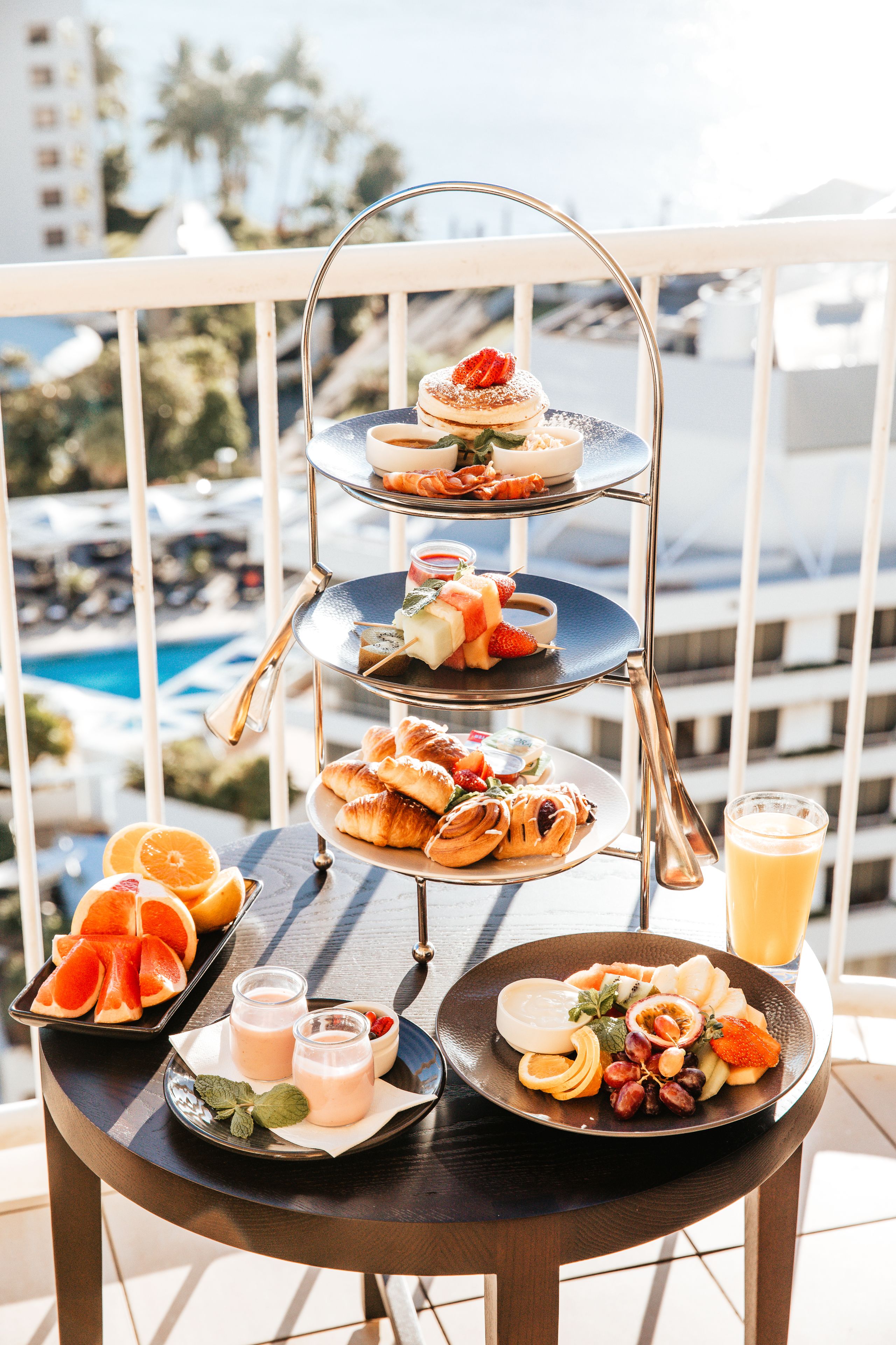 Bandeja de tres niveles con postres en un balcón con vista a la piscina.