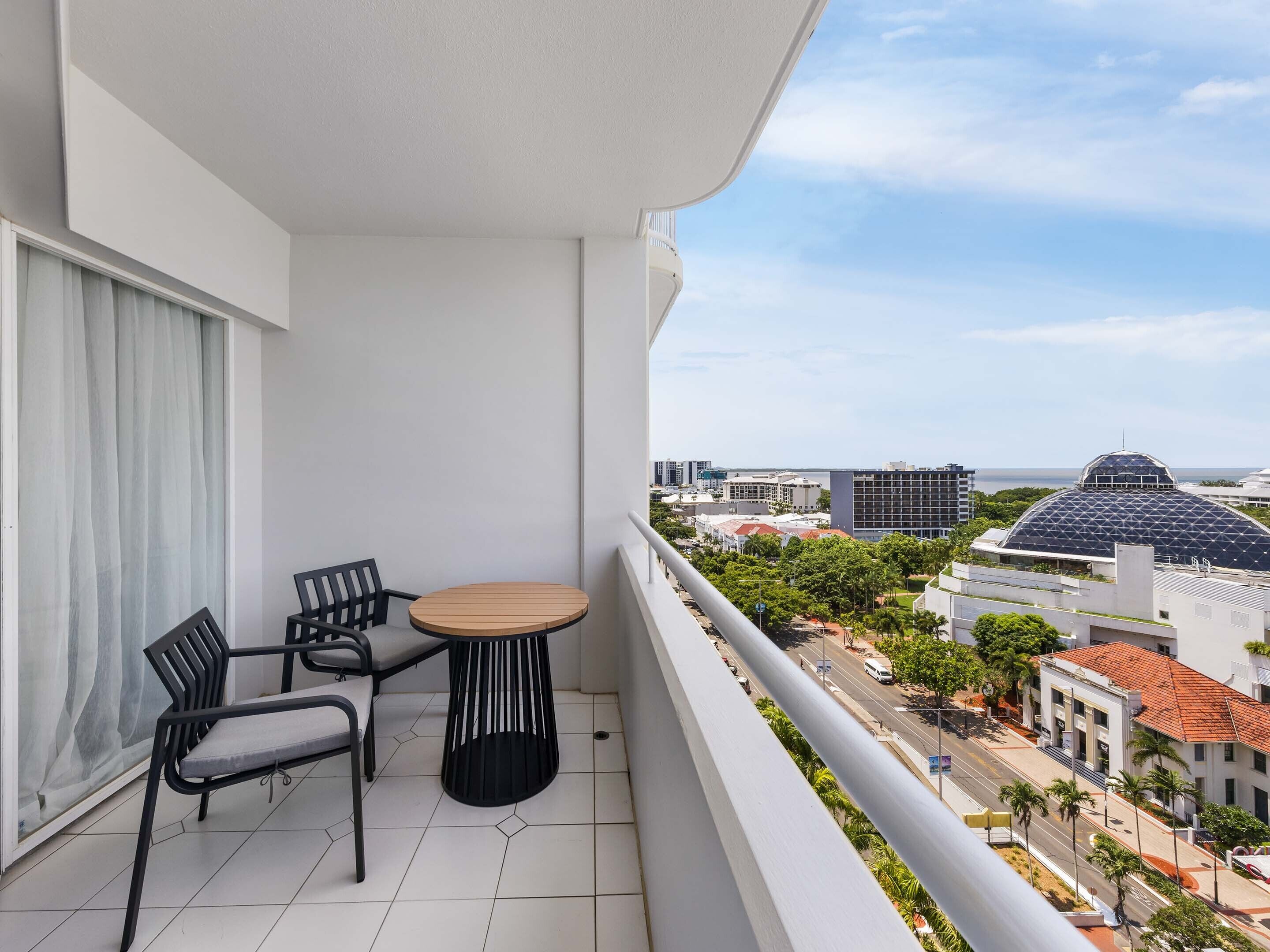 A balcony with a round table and two chairs, overlooking a cityscape with buildings and a dome structure.