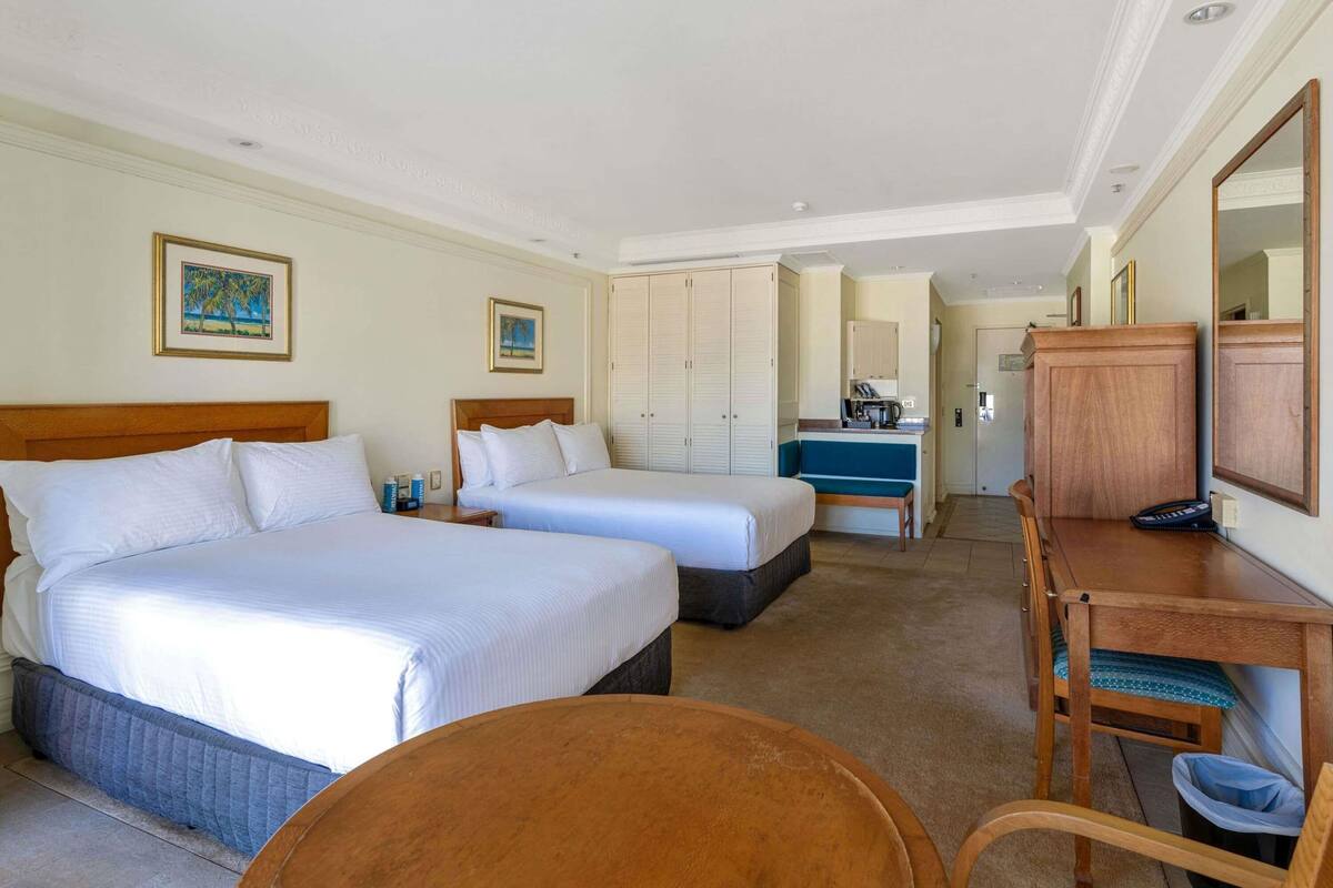 Une chambre d’hôtel avec deux lits, un bureau, une chaise, un miroir et une kitchenette.