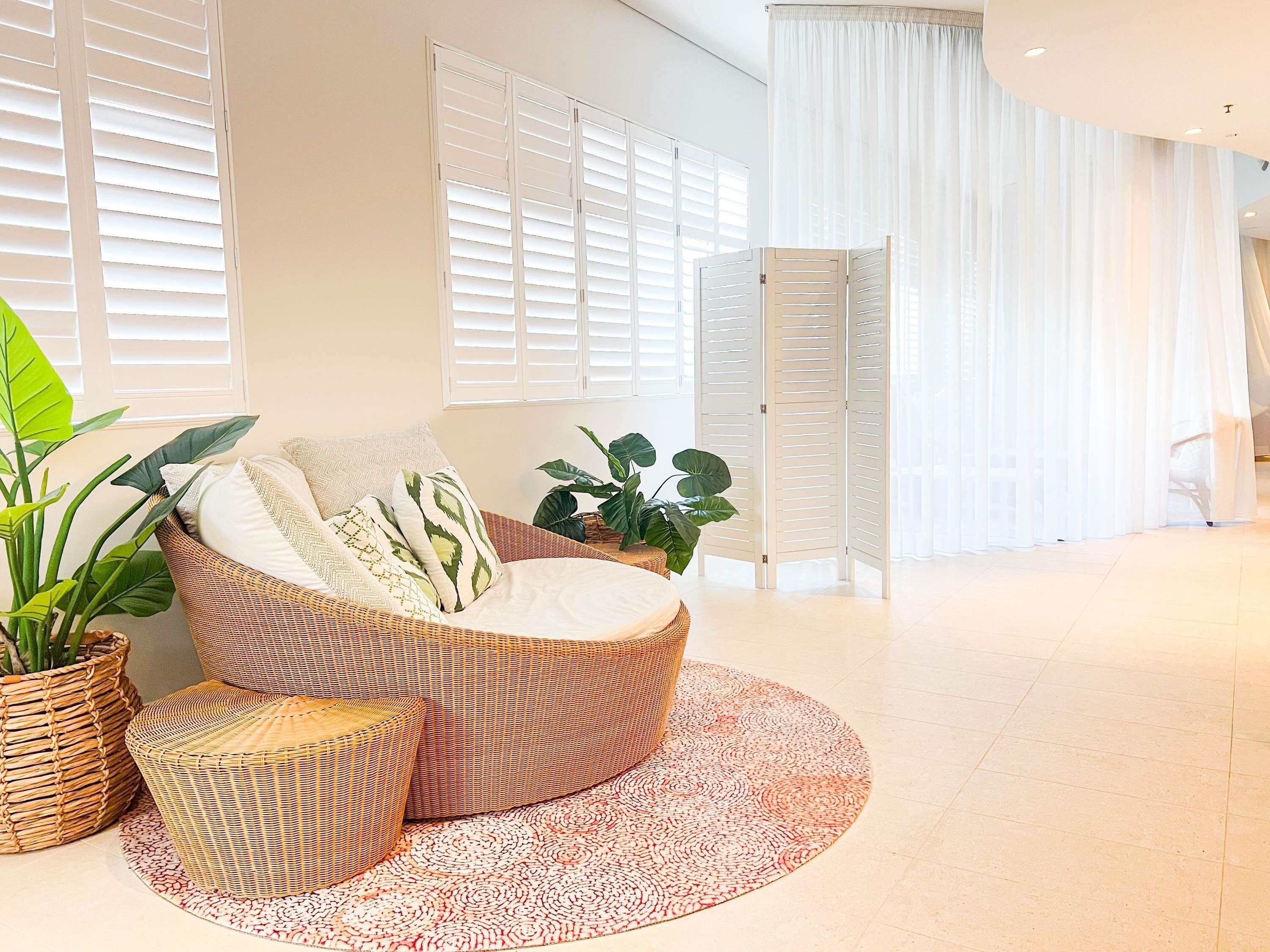 A modern living room with a curved sofa, a round rug, and large windows with white shutters.