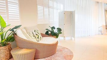 A modern living room with a curved sofa, a round rug, and large windows with white shutters.