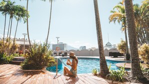A poolside area with palm trees, a wooden deck, and a view of buildings in the background. - Pullman Cairns International (Cairns)