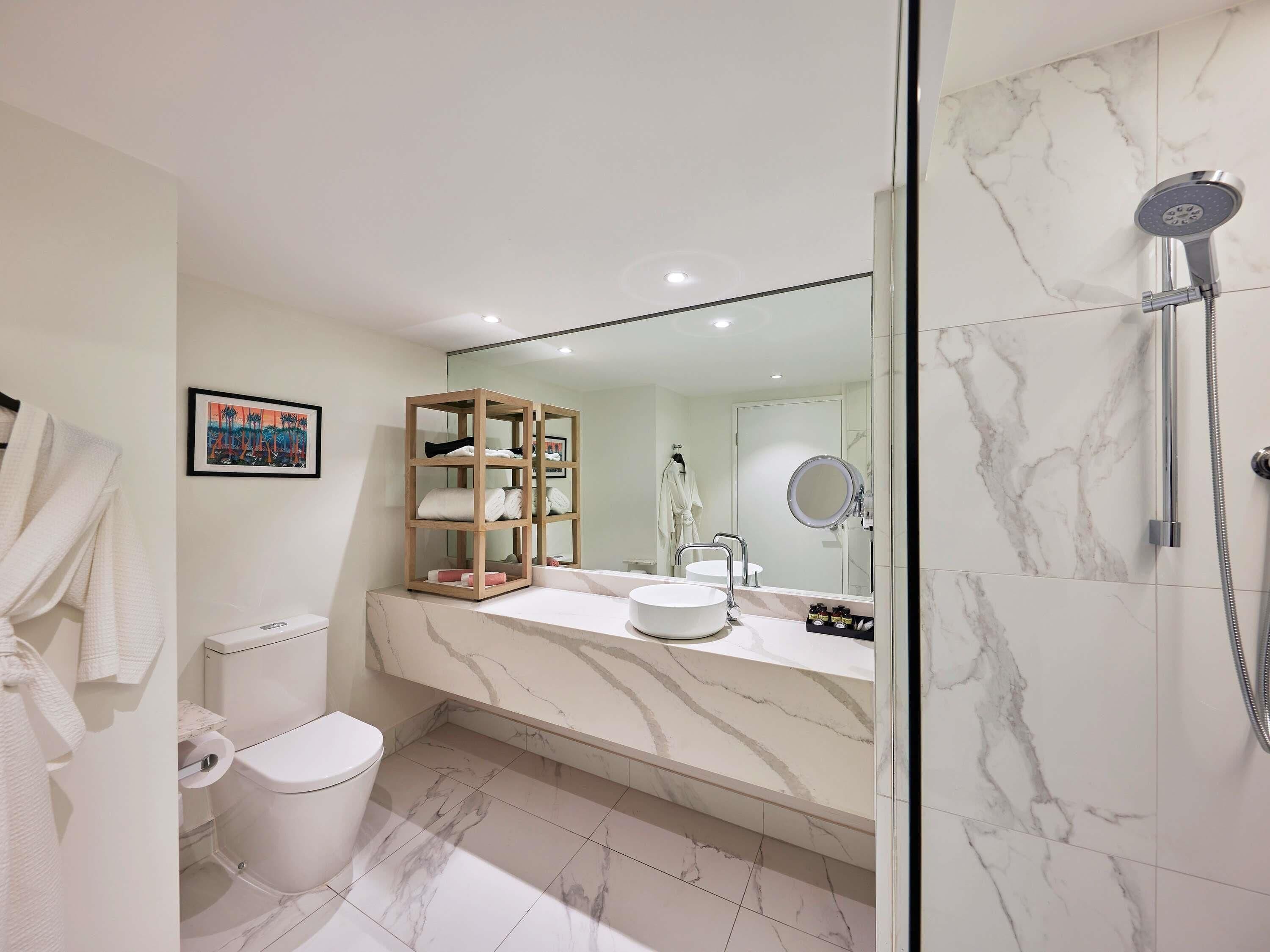 A modern bathroom with a marble floor, a glass shower enclosure, a wooden vanity, and a toilet.