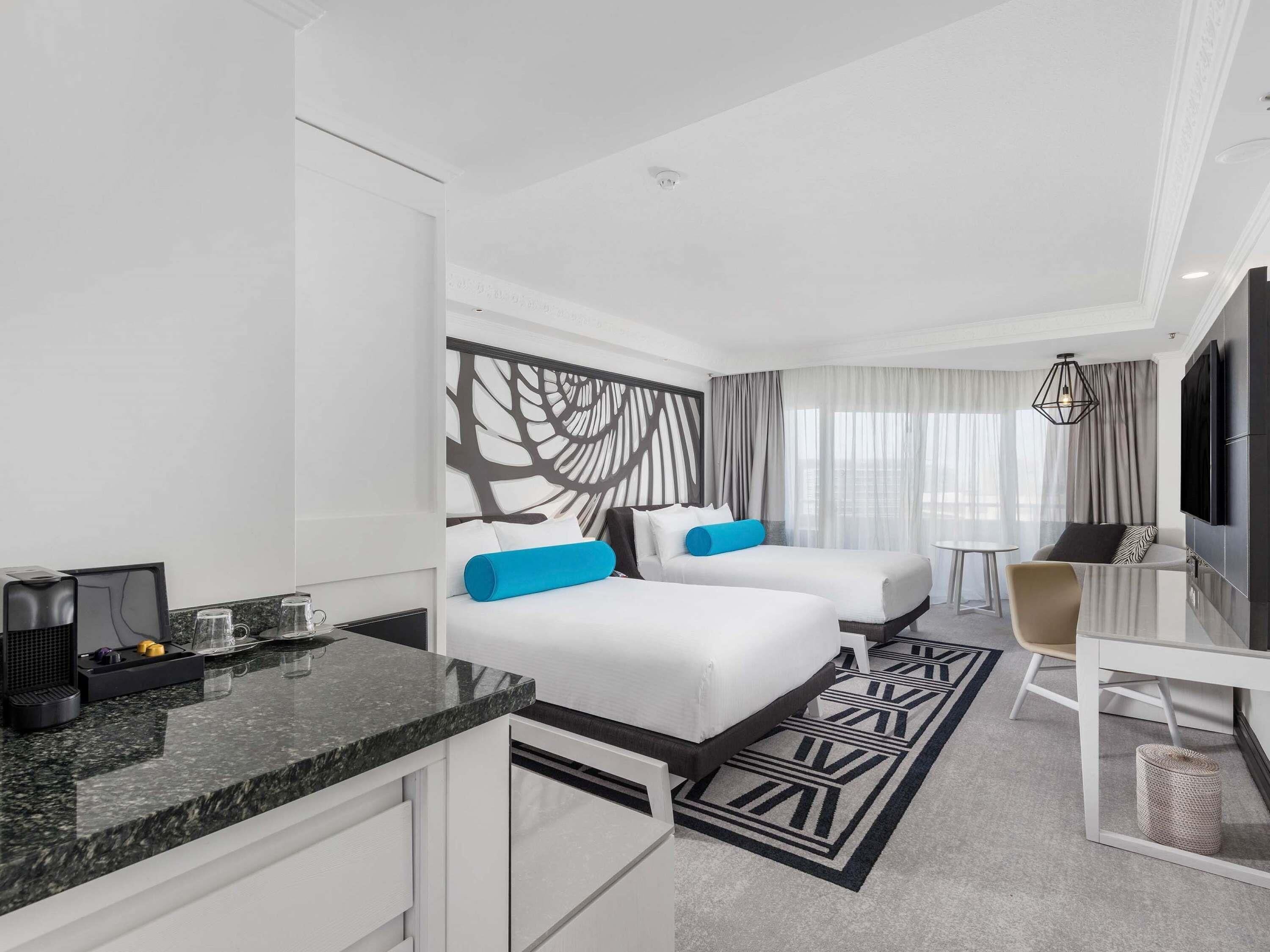 A hotel room with two beds, a desk, a TV, and a coffee machine.
