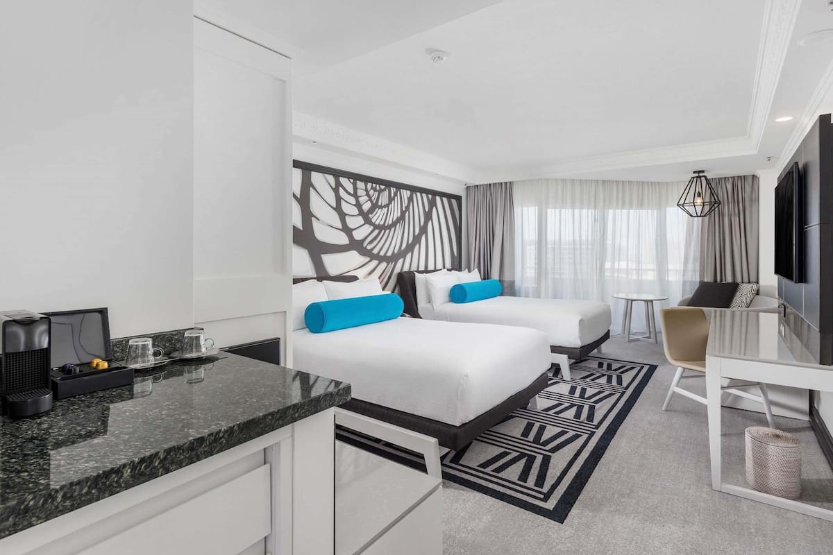 A hotel room with two beds, a desk, a TV, and a coffee machine.