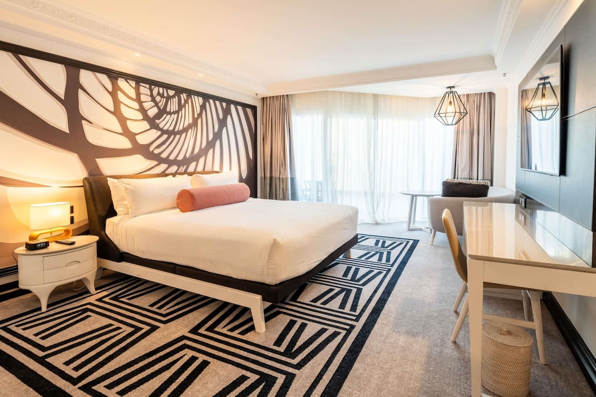 Une chambre d’hôtel moderne équipée d’un lit, d’une table de chevet, d’un bureau et d’un grand miroir.