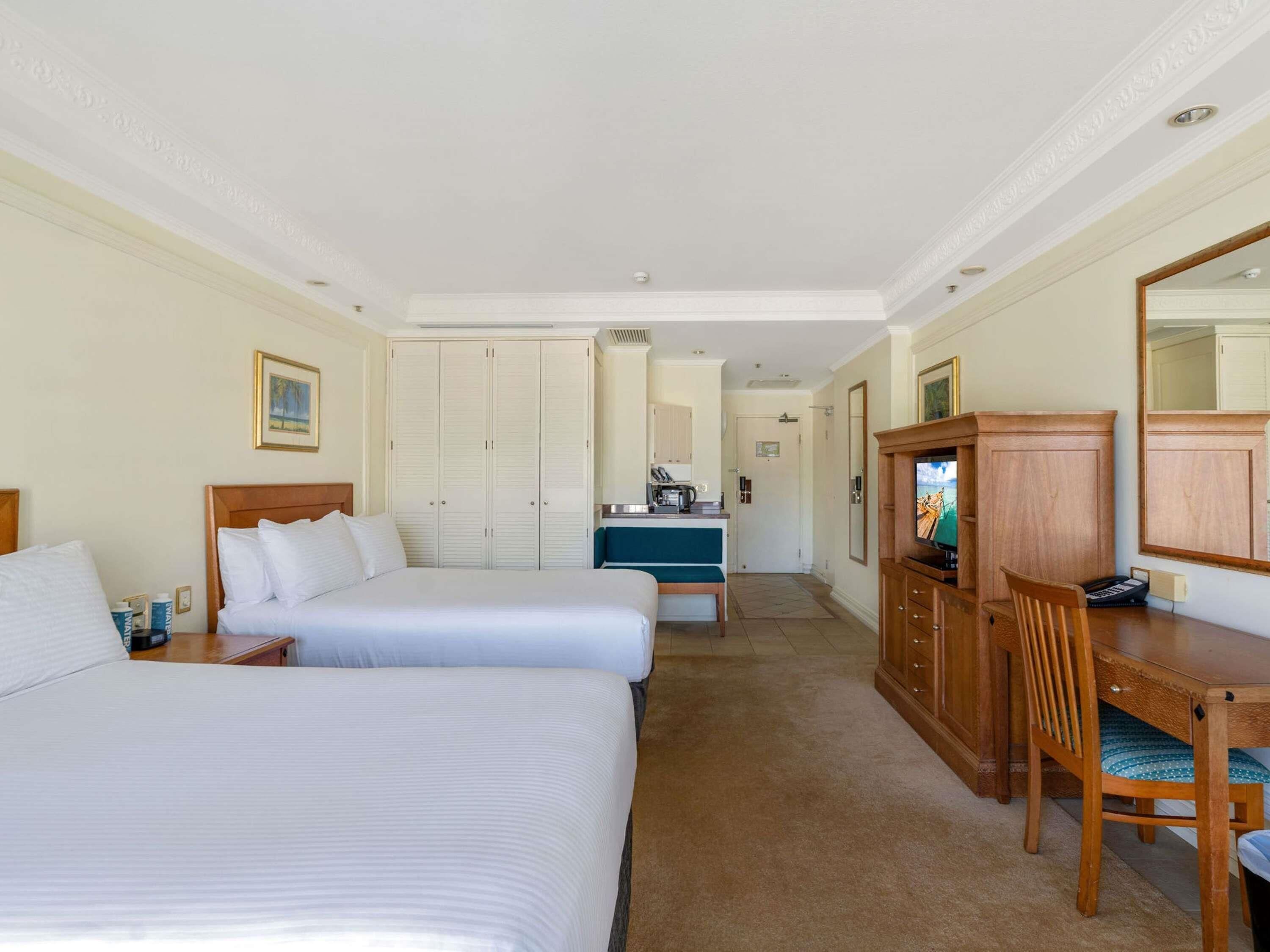 A hotel room with two beds, a desk, a television, and a wardrobe.