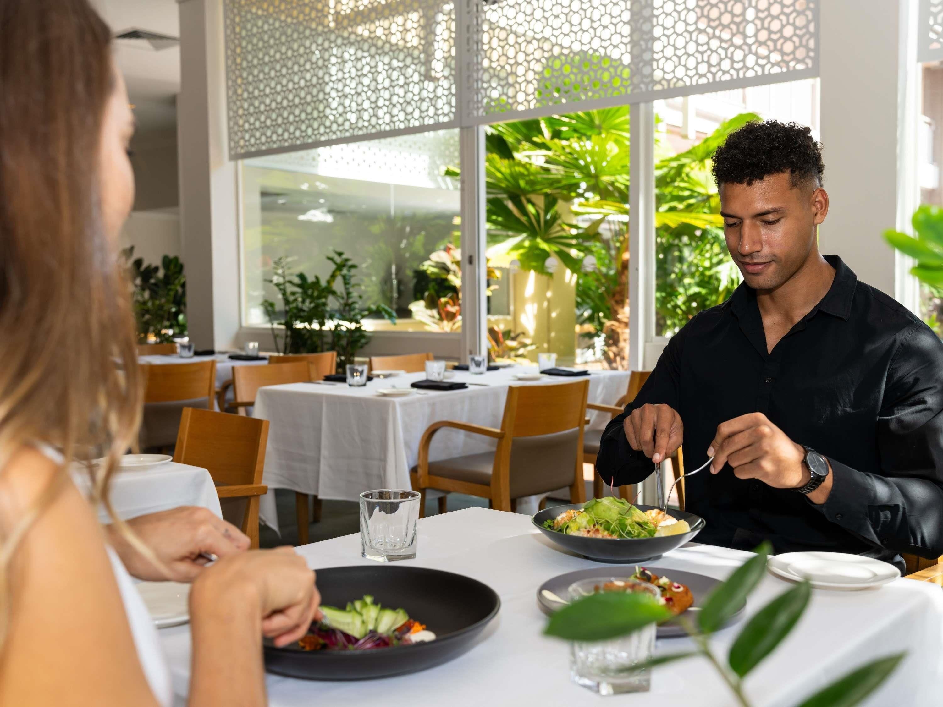 A dining area with tables, chairs, and a view of greenery outside.