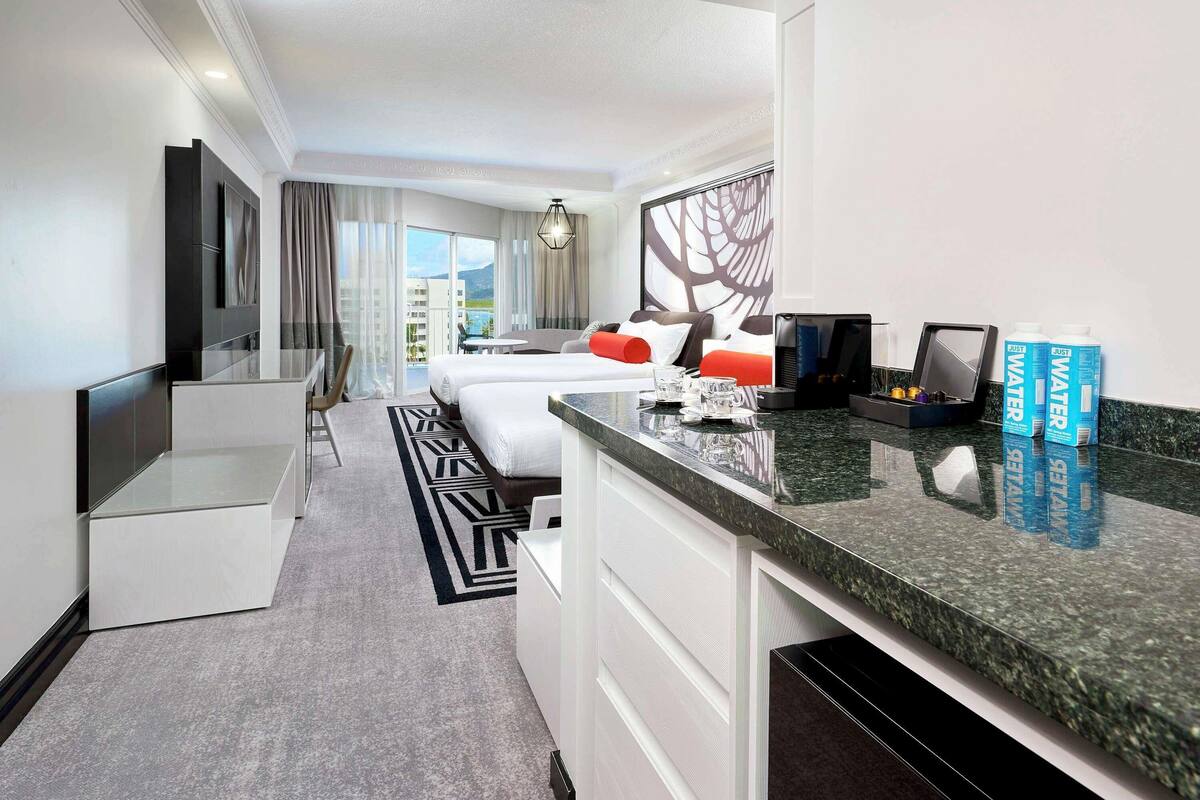 Une chambre d’hôtel comprenant un lit, un bureau, une chaise, une télévision, une fenêtre avec des rideaux et une vue sur des immeubles.
