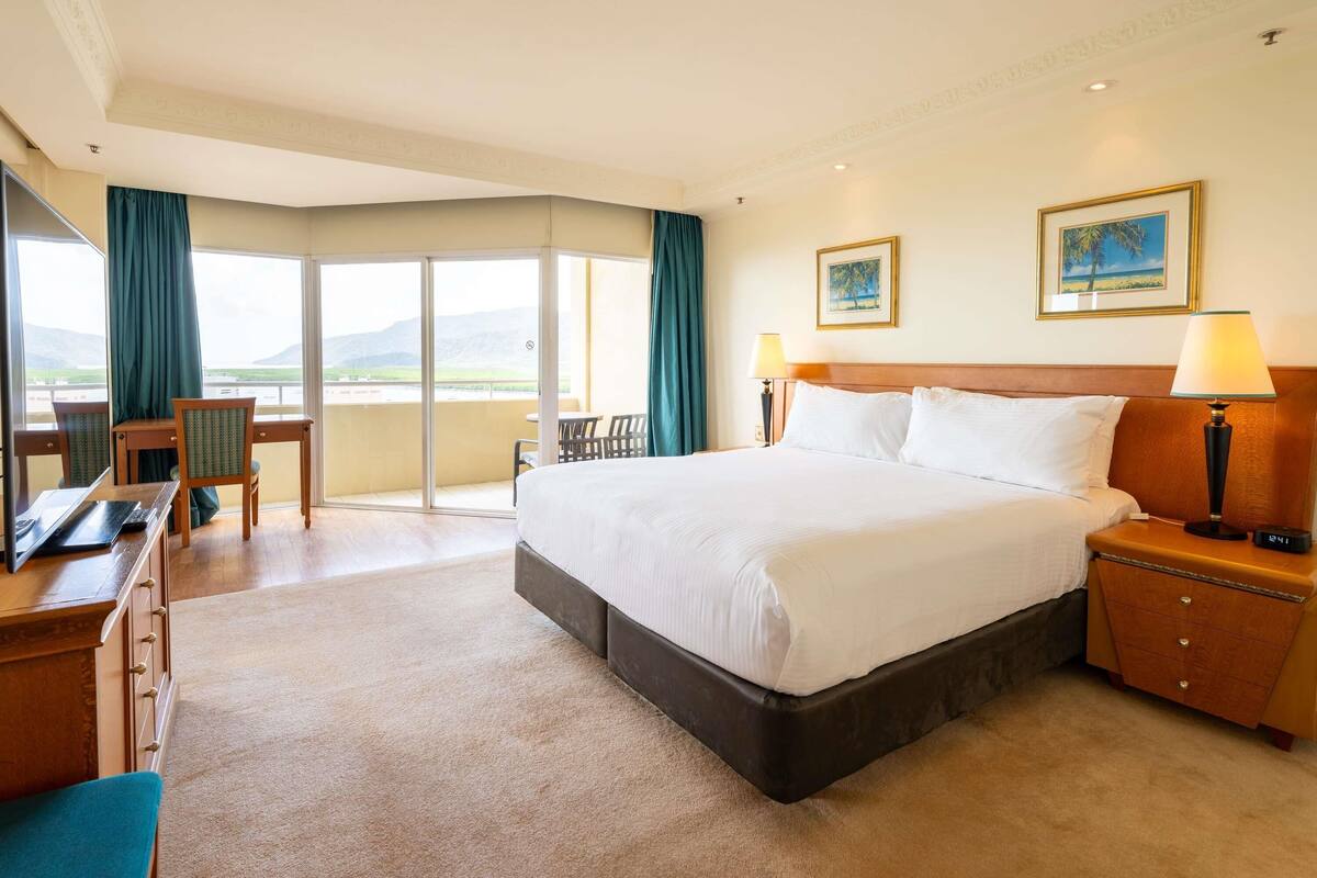 Une chambre d’hôtel avec un lit, un bureau, une chaise et un balcon offrant une vue.