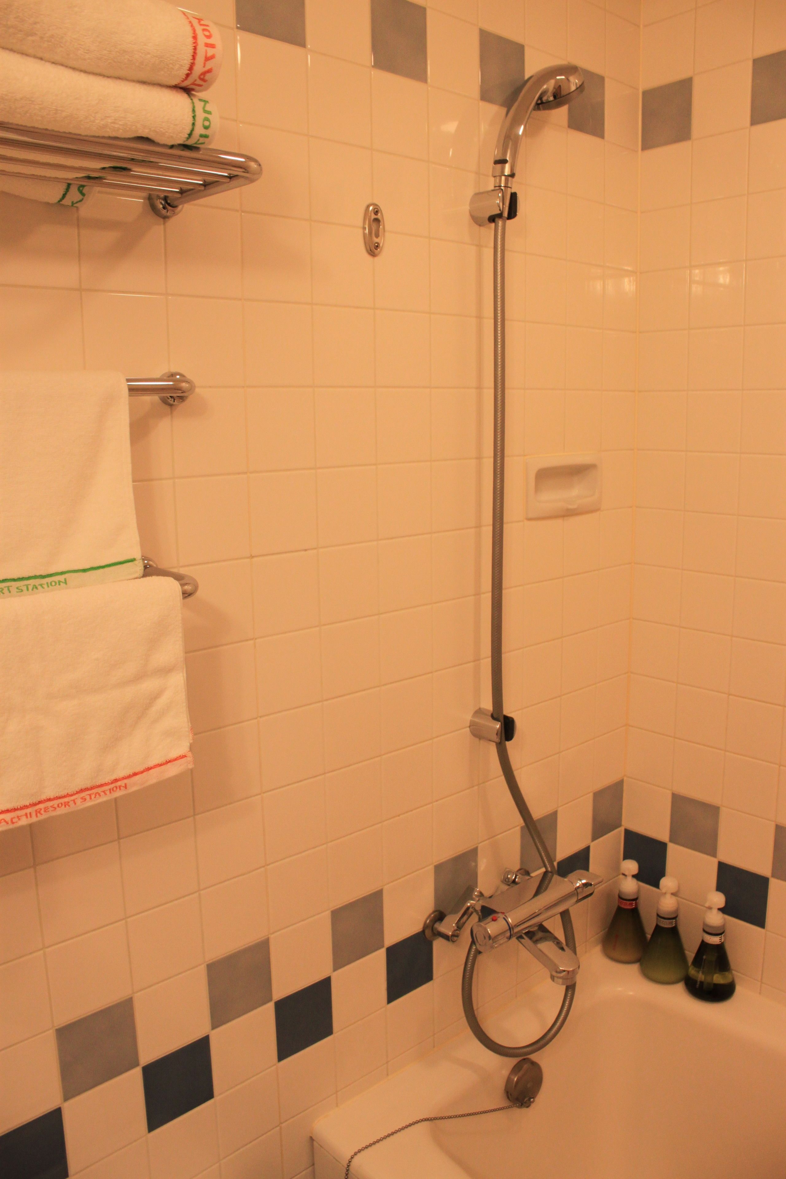 A bathroom with a shower, a towel rack with folded towels, and a soap dispenser.