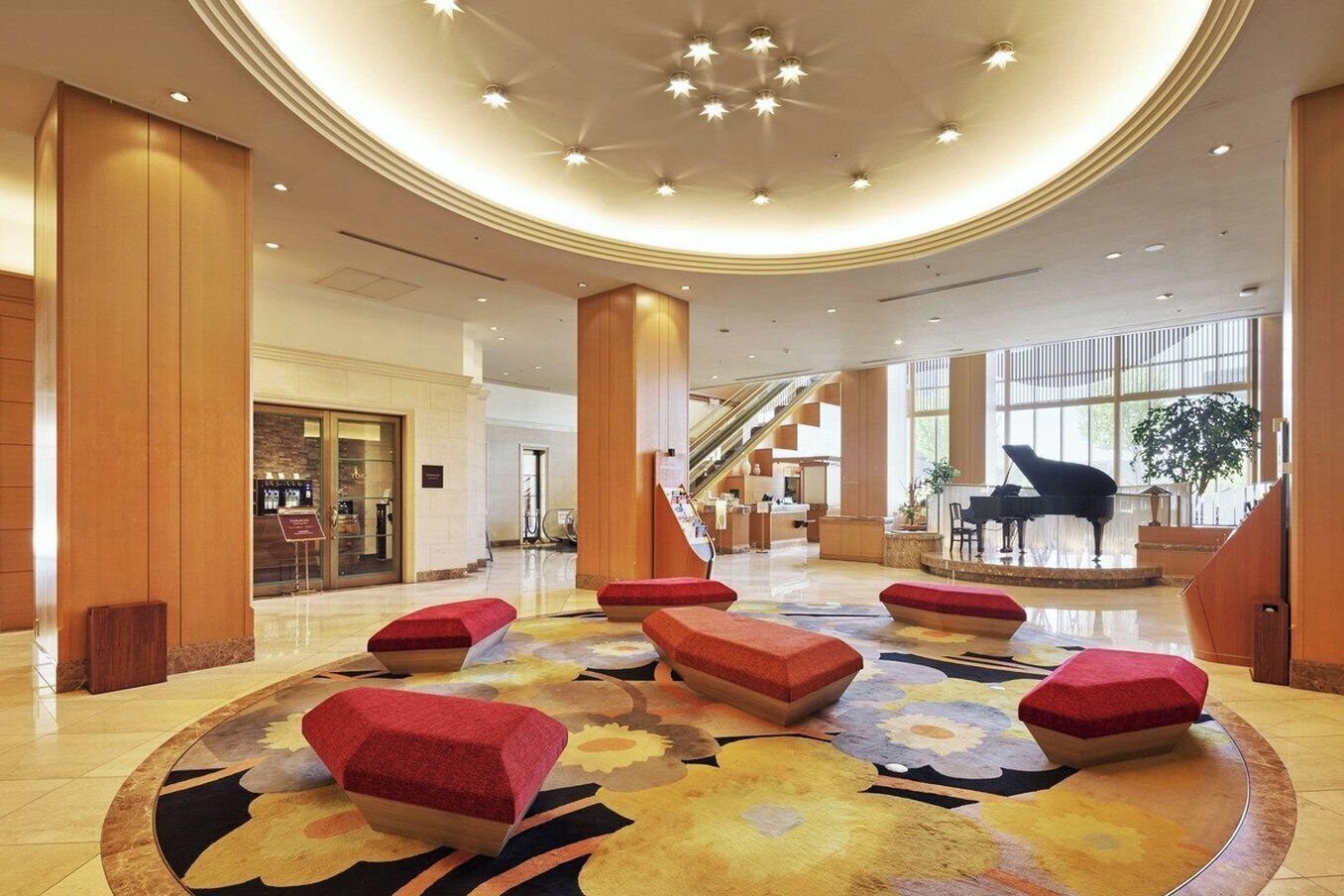 Eine geräumige Lobby mit einer imposanten Treppe, einem Klavier und einer zentralen Sitzecke mit roten Kissen.