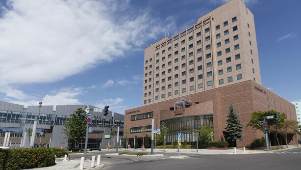 Un hotel moderno con fachada de ladrillo y grandes ventanales, ubicado en una intersección urbana con semáforos y señales de tráfico.