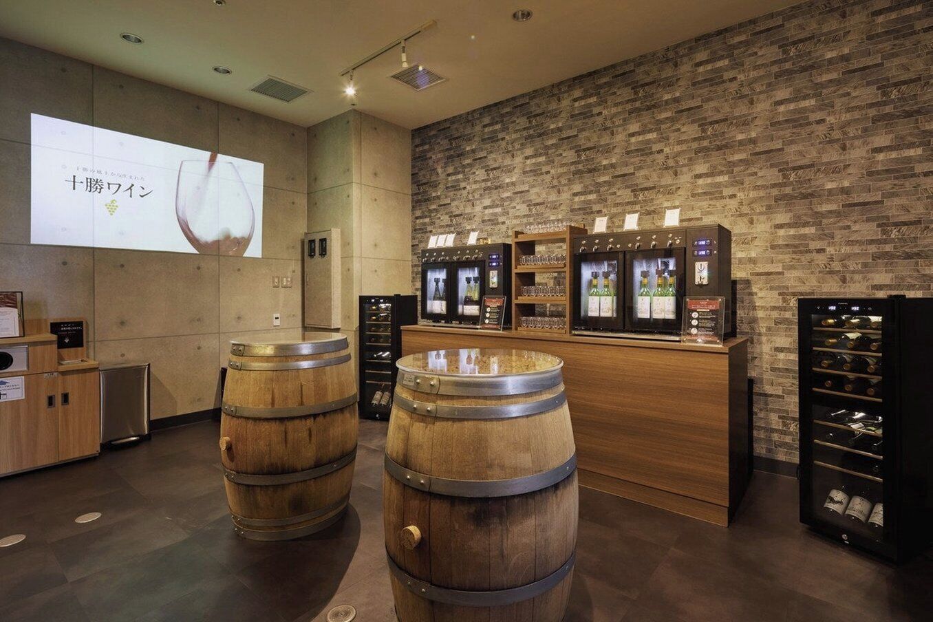 A bar area with wooden barrels, a projection screen, and wine refrigerators.