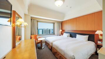 A hotel room with two beds, a desk, a chair, a small table, and a large window with a city view.