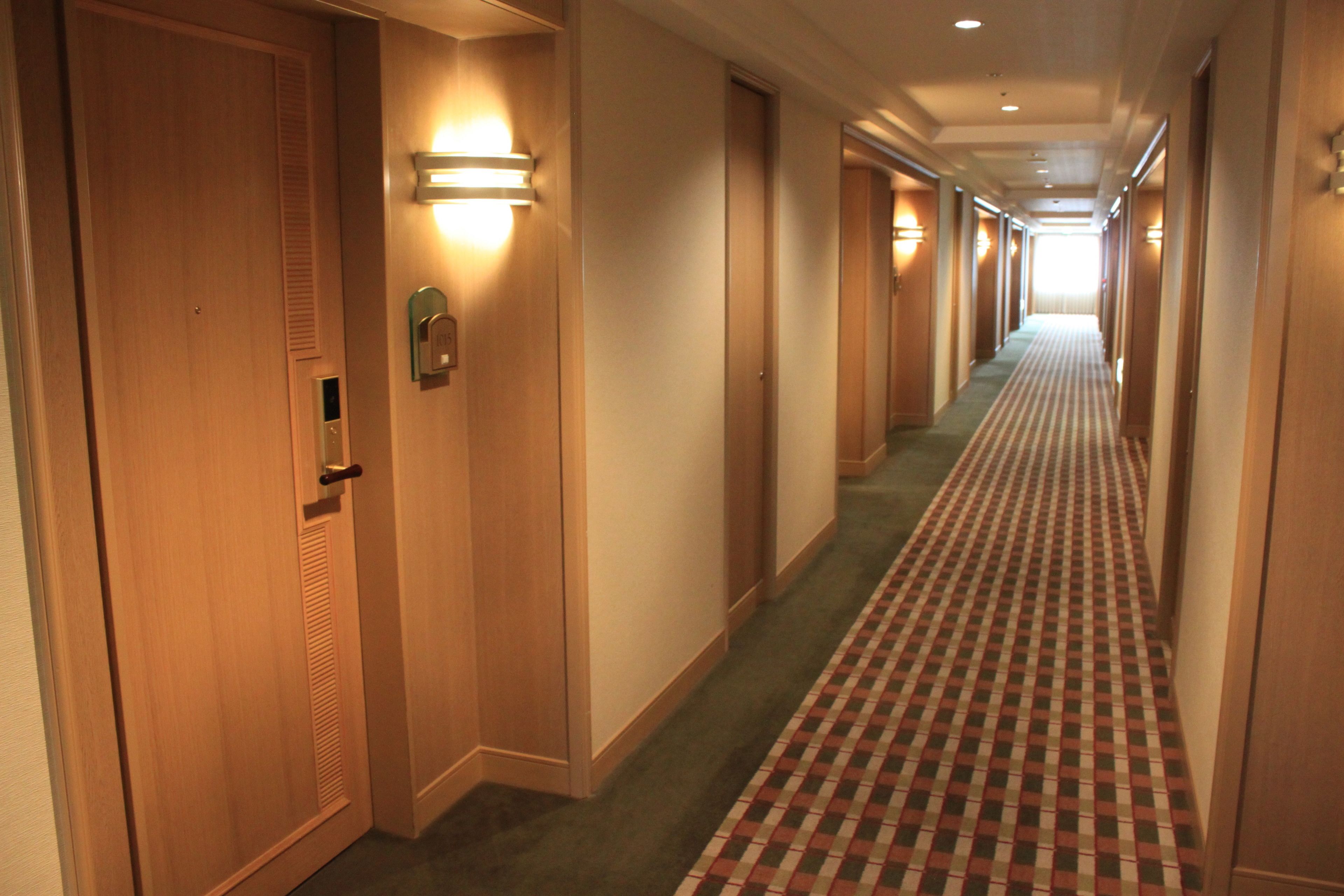 Een hotelgang met houten deuren, een geruit tapijt en wandlampen.