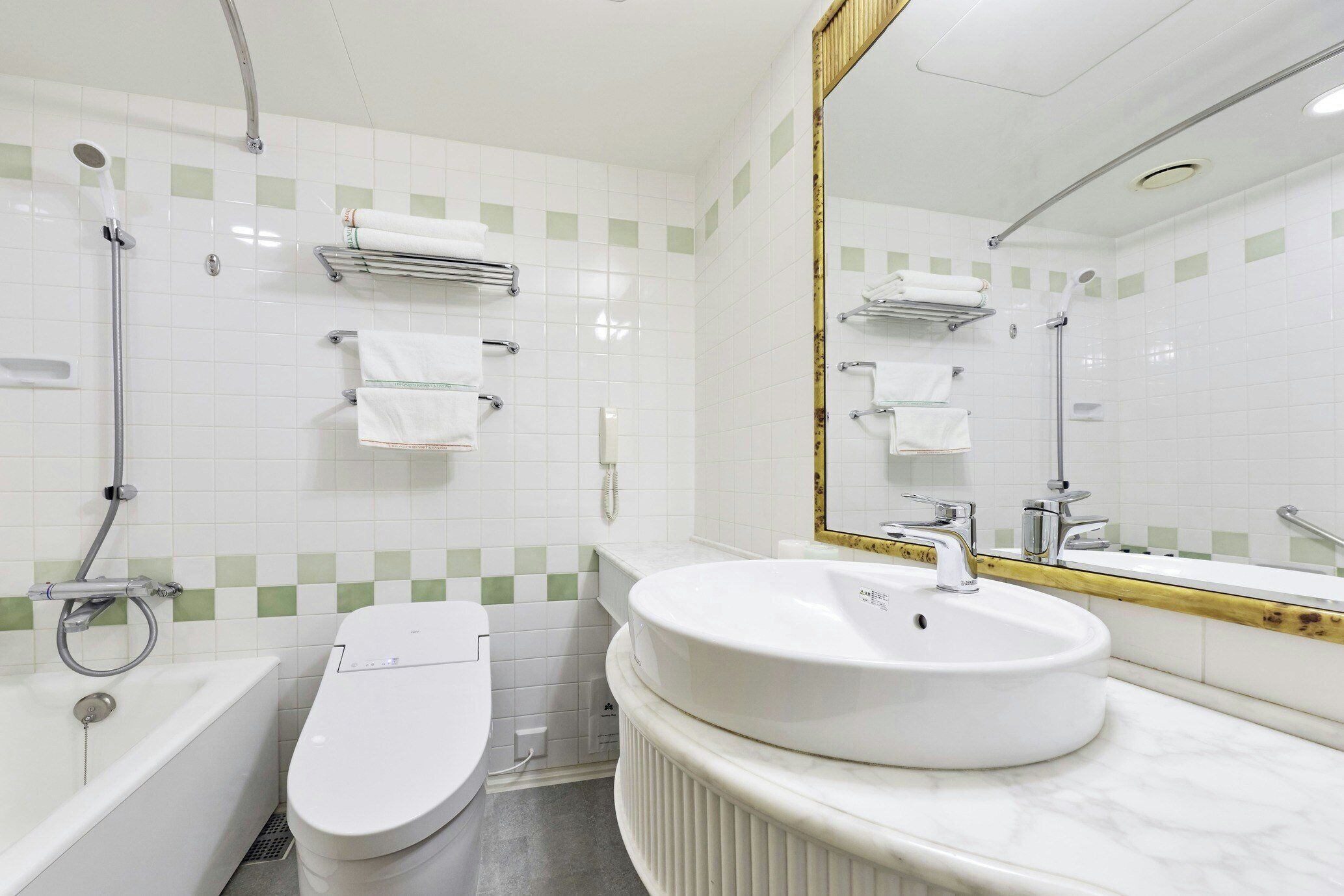 A bathroom with a bathtub, toilet, and sink, featuring white fixtures and green-tiled walls.