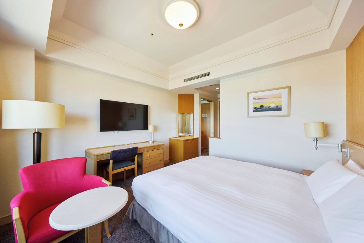 Une chambre d’hôtel avec un lit, un bureau, une chaise, une télévision et un tableau au mur.