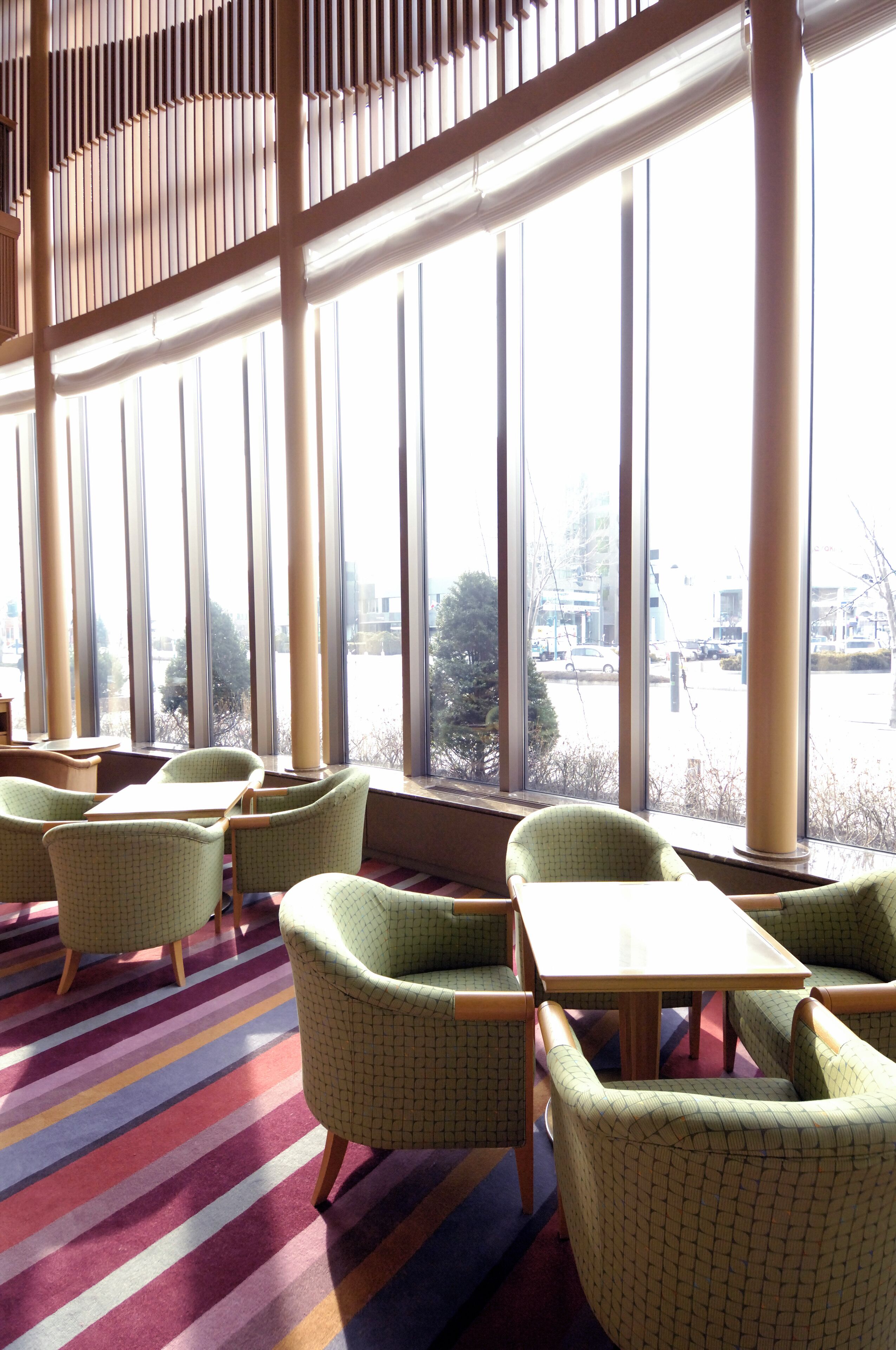 A room with large windows, green upholstered chairs, and a striped carpet.