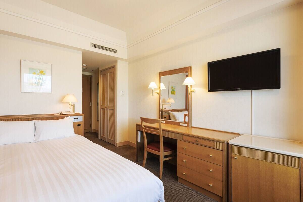 Une chambre d’hôtel comprenant un lit, un bureau, une chaise, un miroir, une télévision et une porte donnant sur une autre pièce.