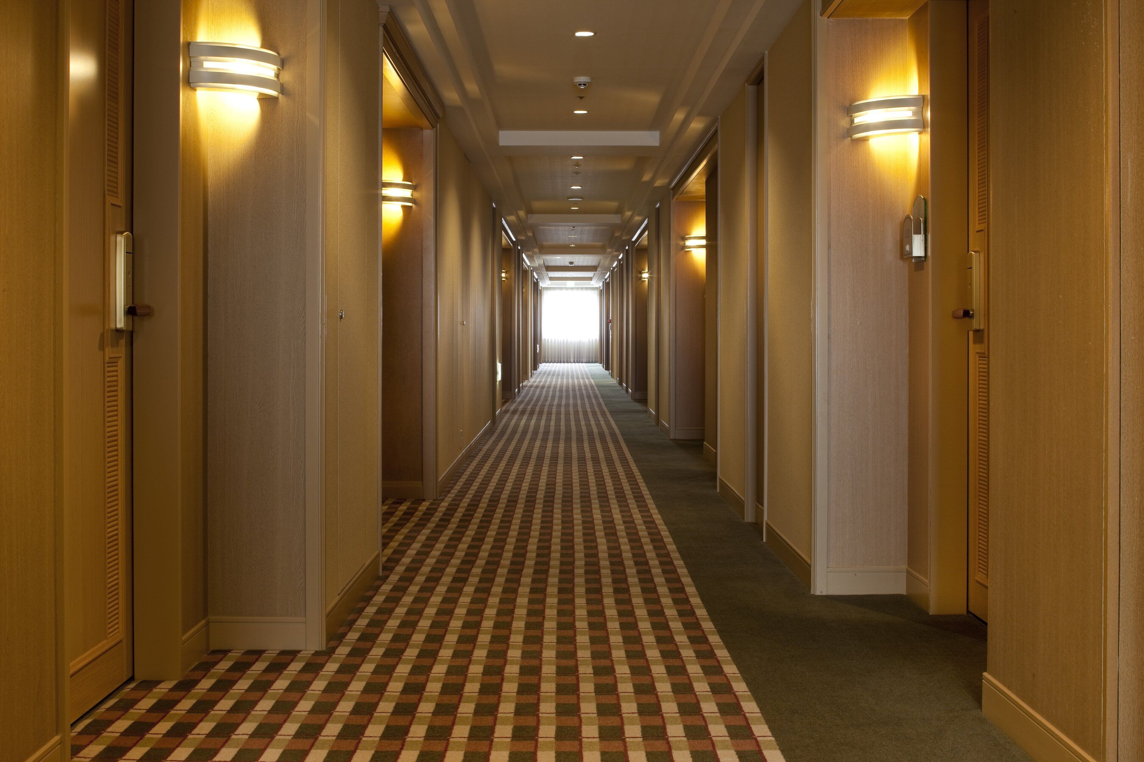 Ein Hotelkorridor mit Schachbrettmuster-Teppich, Holzwänden und Wandleuchten.