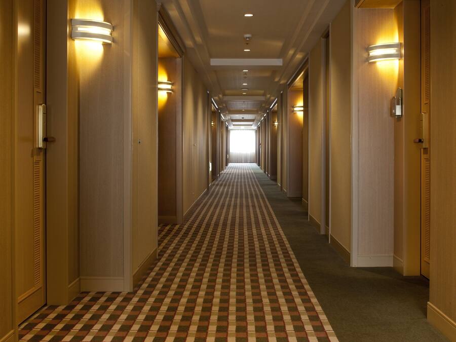 Ein Hotelkorridor mit Schachbrettmuster-Teppich, Holzwänden und Wandleuchten.