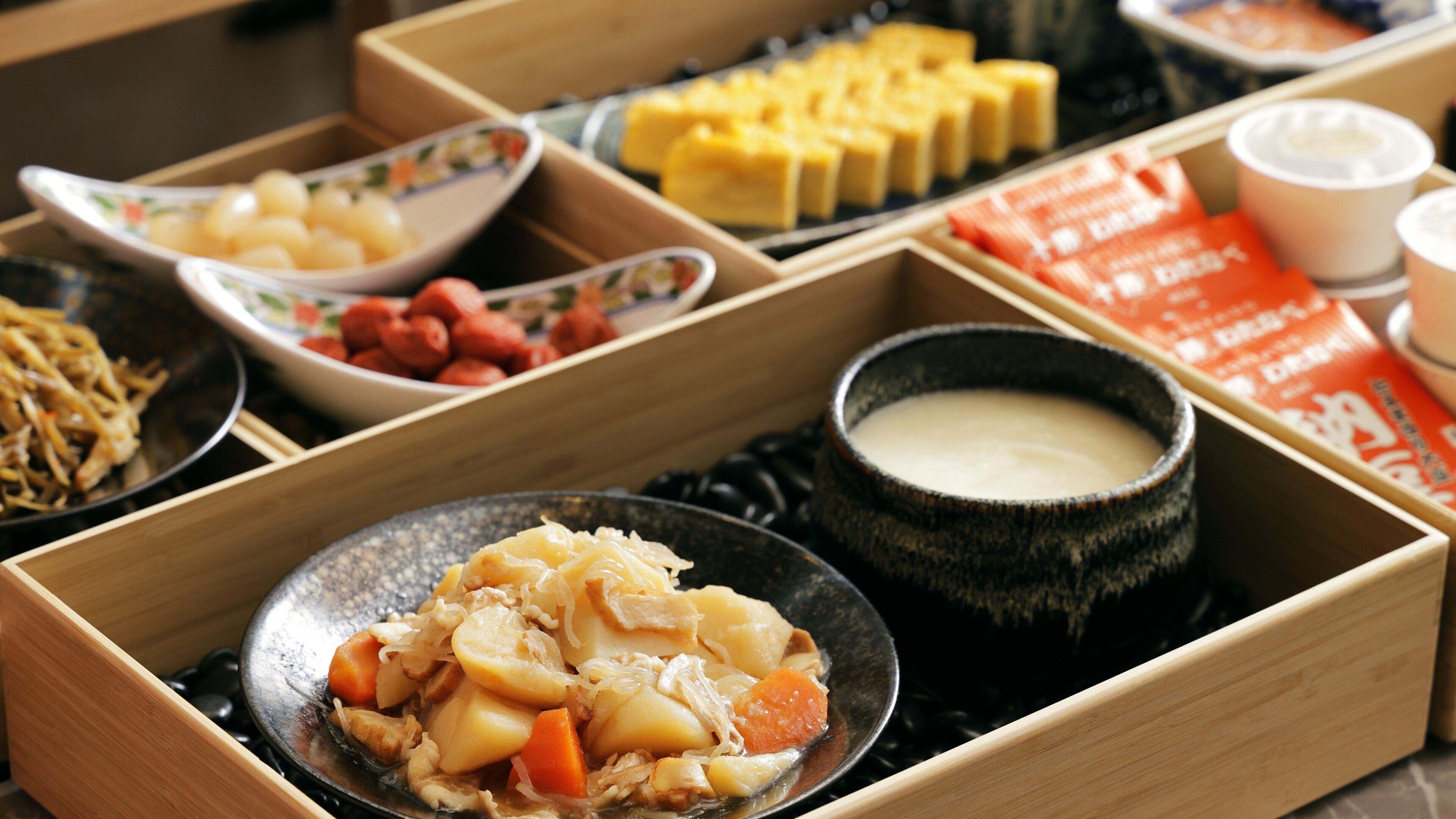A variety of dishes in wooden boxes, including a bowl of mixed vegetables and a small bowl of soup.