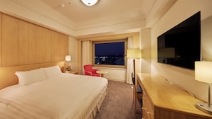 Habitación de hotel con una cama grande, un escritorio, una silla, un televisor y una ventana con vista a la ciudad.