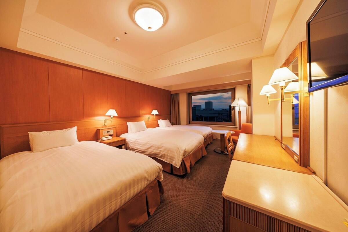 Une chambre d’hôtel avec deux lits, un bureau et un grand miroir.